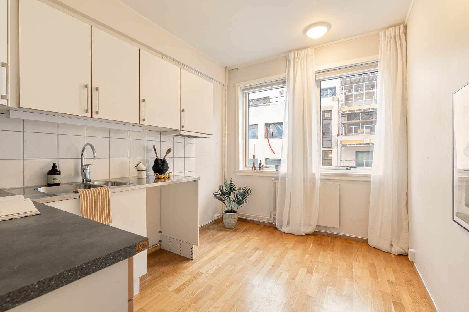 Separat kjøkken med Tvis-innredning fra 2018 med glatte hvite fronter, laminatbenkeplate og benkeplate beslått i børstet stål med innfelt 1,5 vaskekum og ettgreps armatur fra Oras Galleribilde