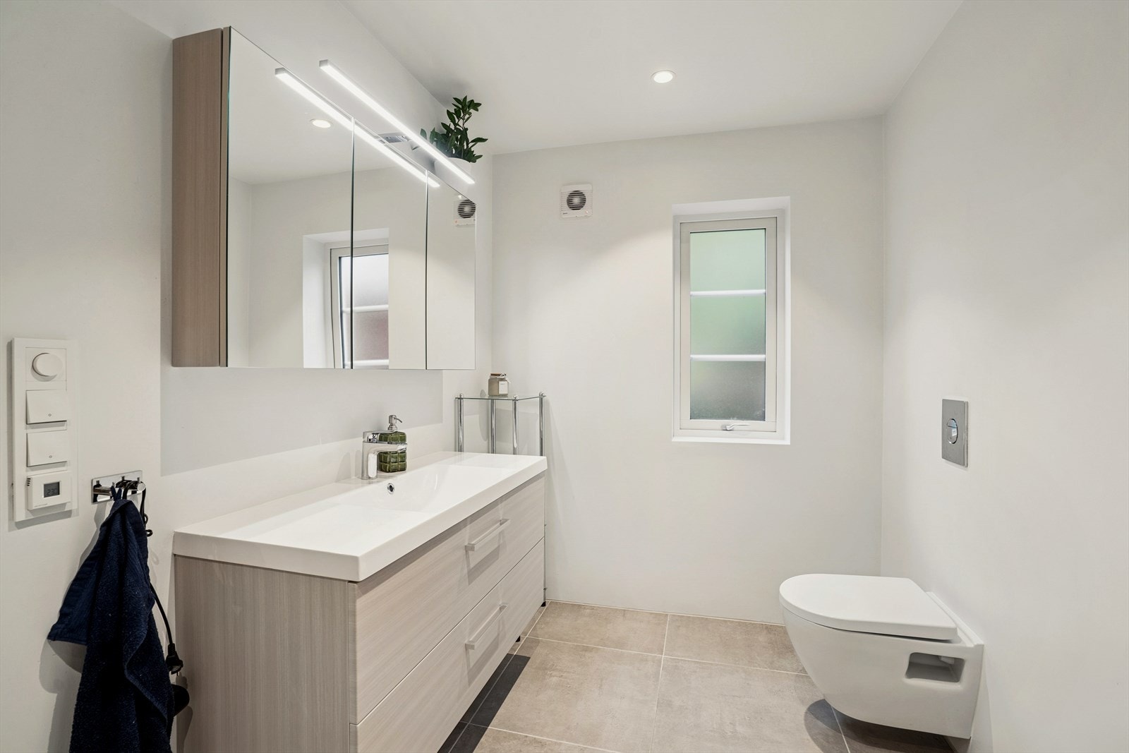 Badet er utstyrt med vegghengt klosett, servant med skuffer, speil overskap. Det er opplegg for vaskemaskin og elektrisk styrt vifte. Galleribilde