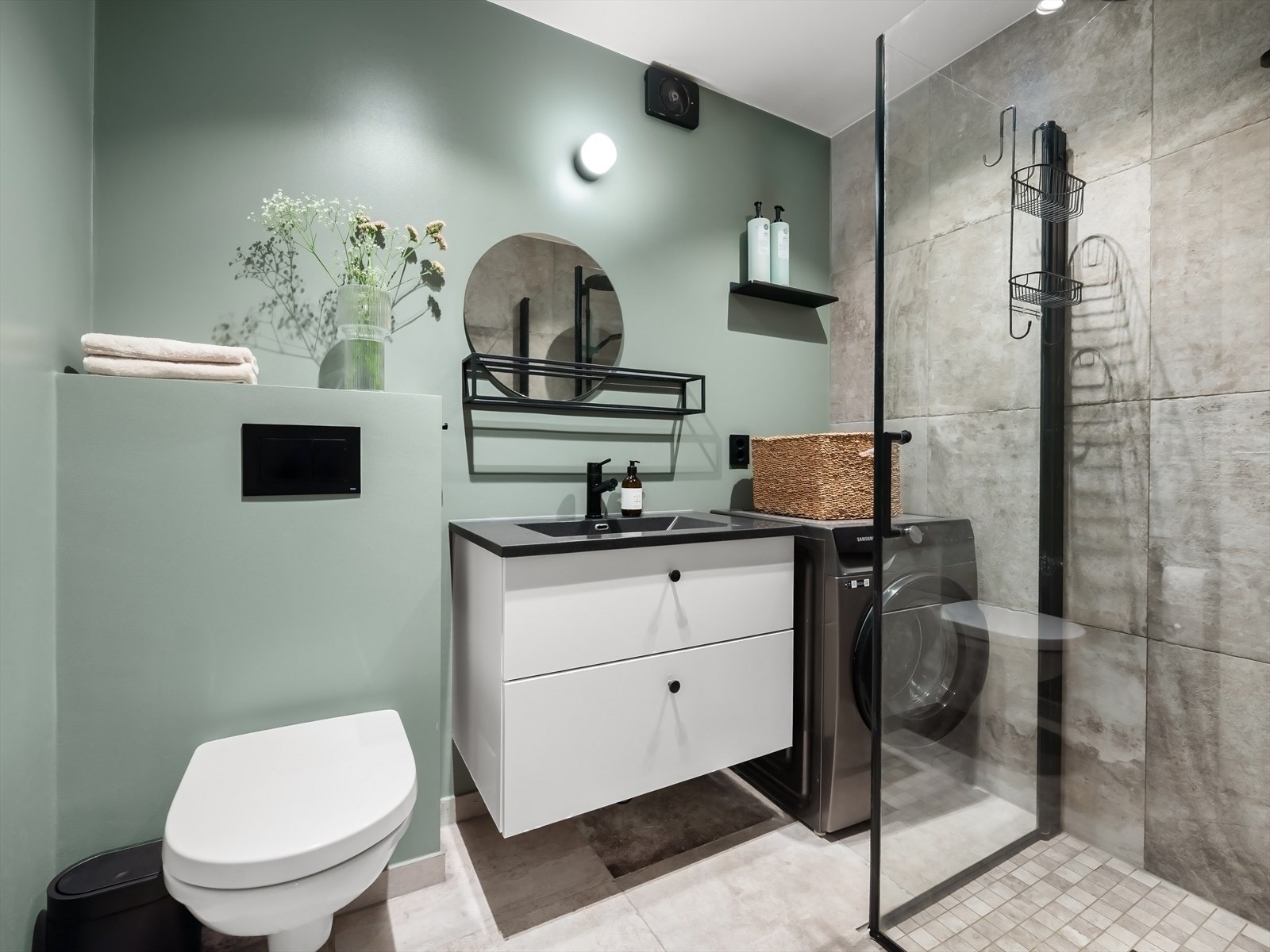 Badet har regnfalldusj, servantinnredning med skuffer, opplegg for vaskemaskin og veggmontert toalett. Galleribilde