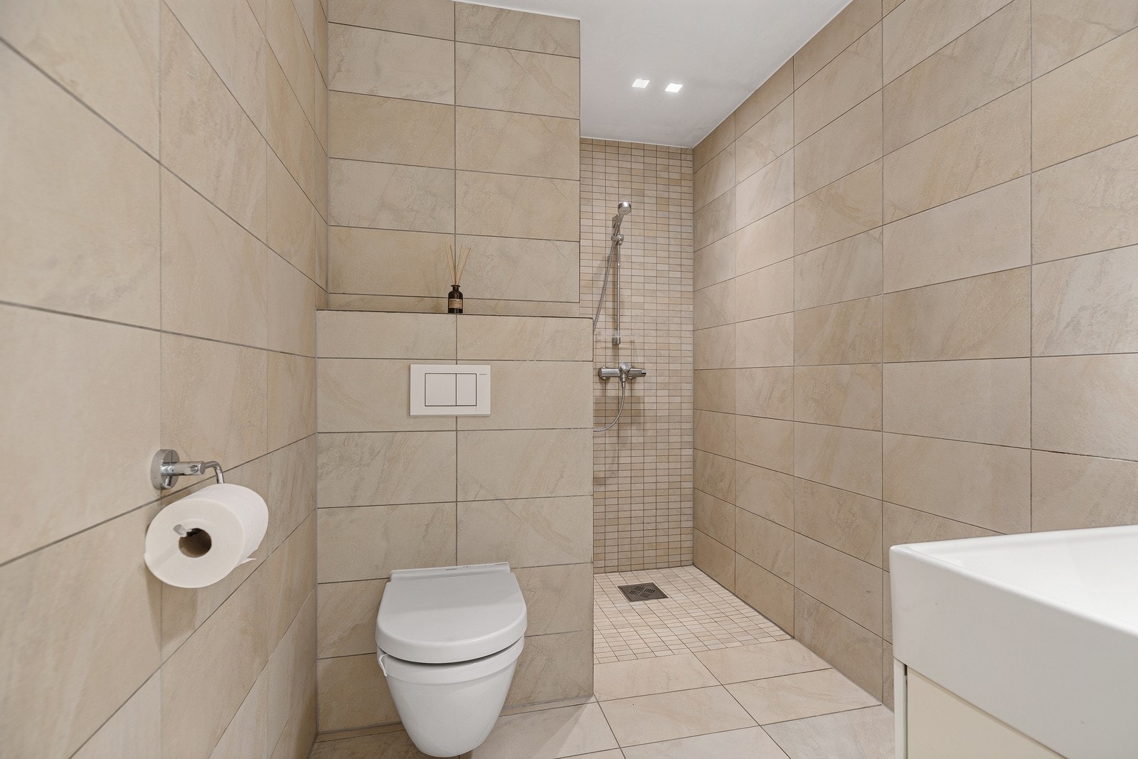 Flislagt bad med dusjnisje og vegghengt toalett. Galleribilde