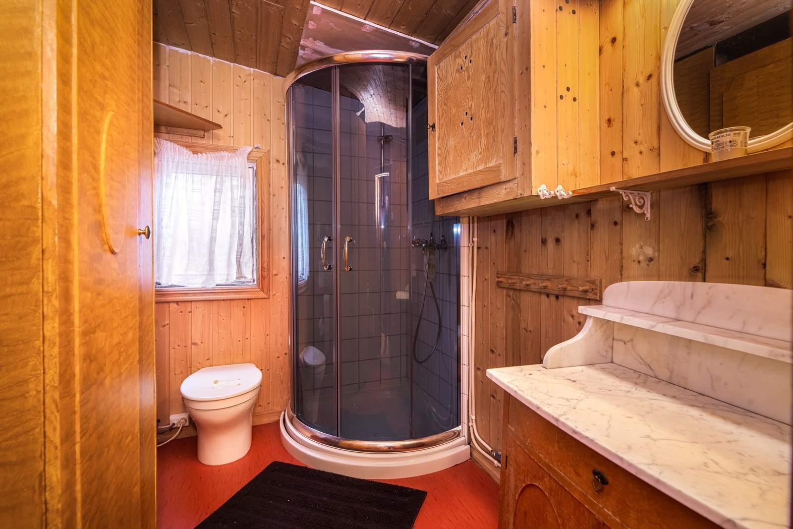 Badet innehar servantskap med løs vask, biotoalett og dusj på vegg med dusjvegger. Det er montert panelovn på vegg. Galleribilde