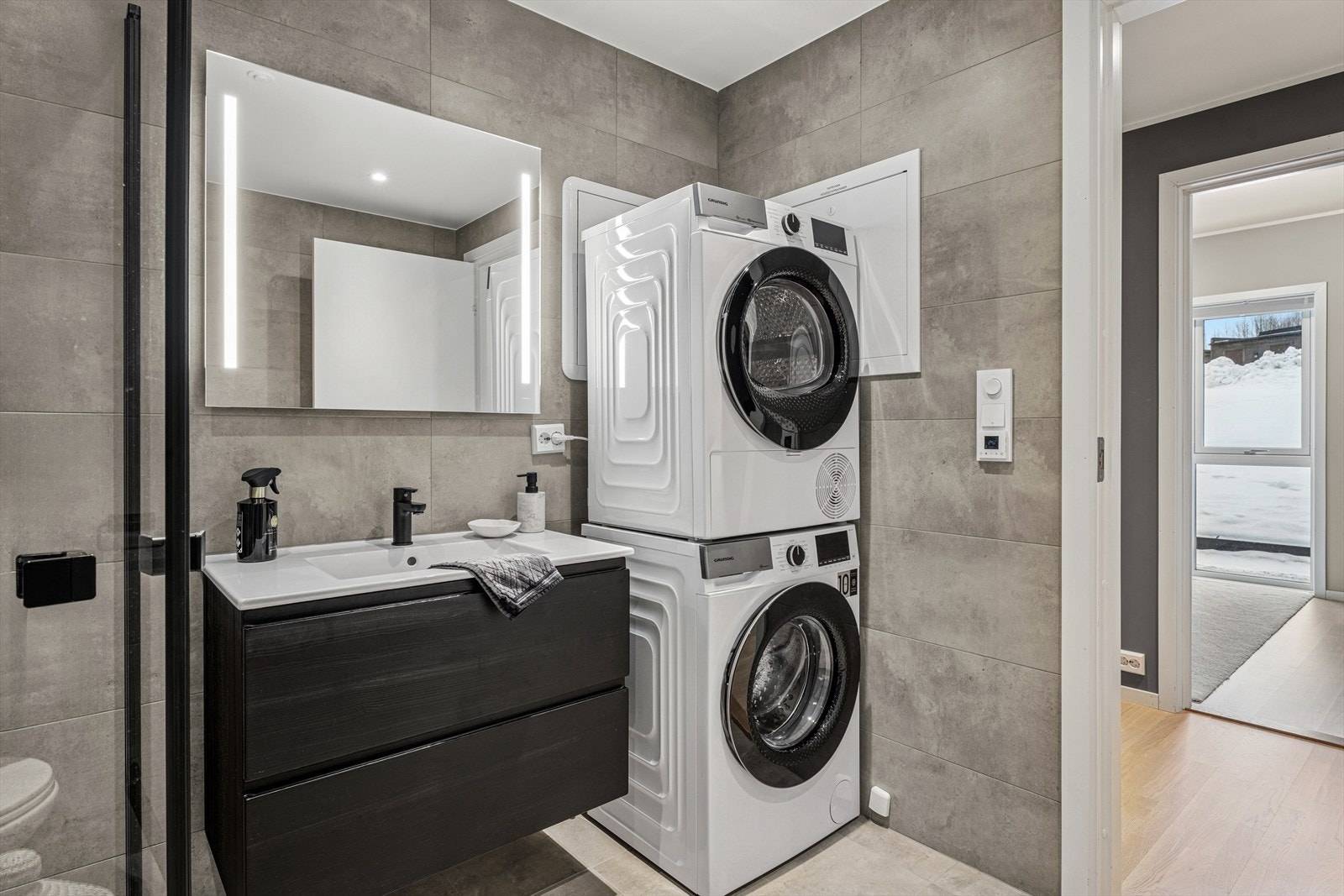 Lekkert bad med moderne servantinnredning, glassdusj med både regn- og hånddusj, vegghengt toalett og opplegg for vaskemaskin. Fliser, varmekabler og downlights gir et stilrent og behagelig uttrykk. Galleribilde