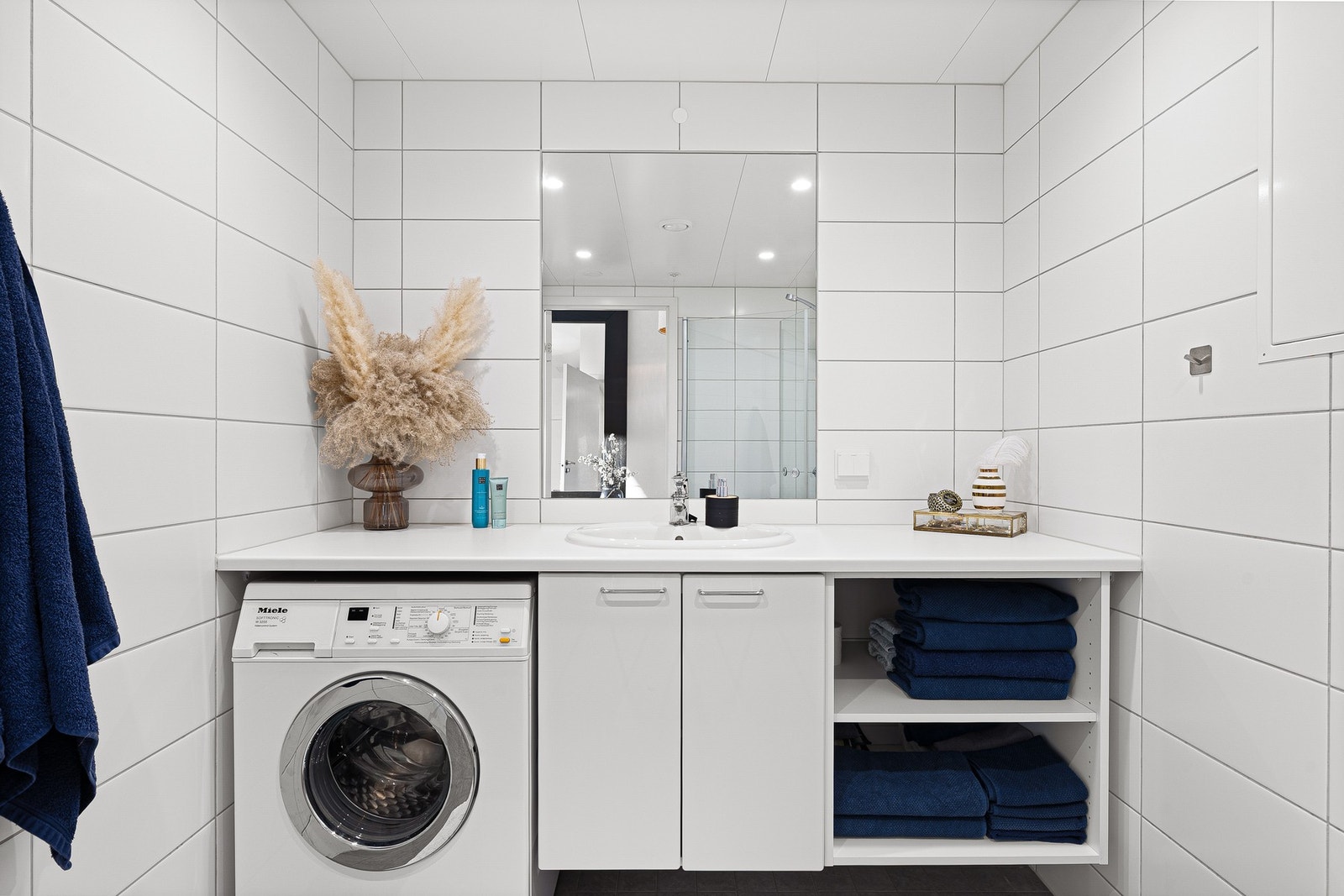 Badet er utstyrt med kran og avløp for vaskemaskin, innfellbare og plassbesparende dusjdører i glass, vegghengt toalett og servant med underskap. Spotter i himling. Galleribilde