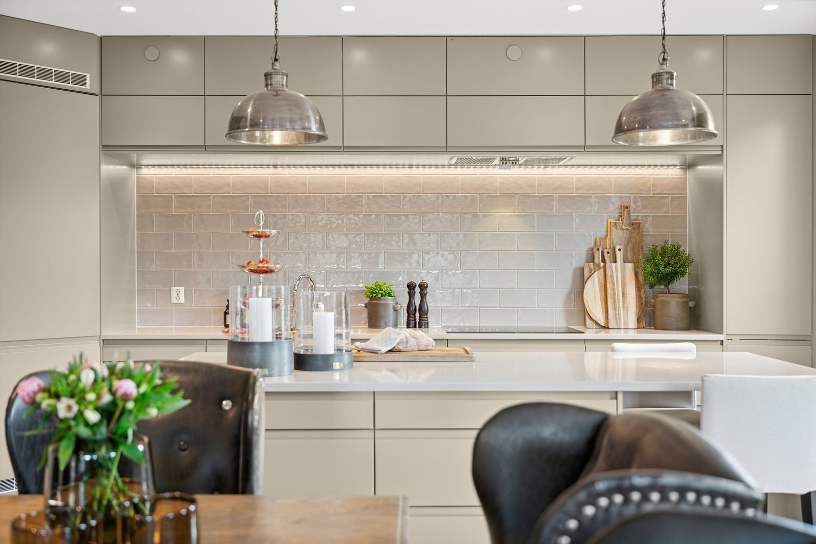 Kjøkkenet fremstår gjennomført med overskap, benkeplate i komposittstein med underlimt stålkum og flislagt bakvegg, en stilren kombinasjon av funksjon og finesse. Galleribilde