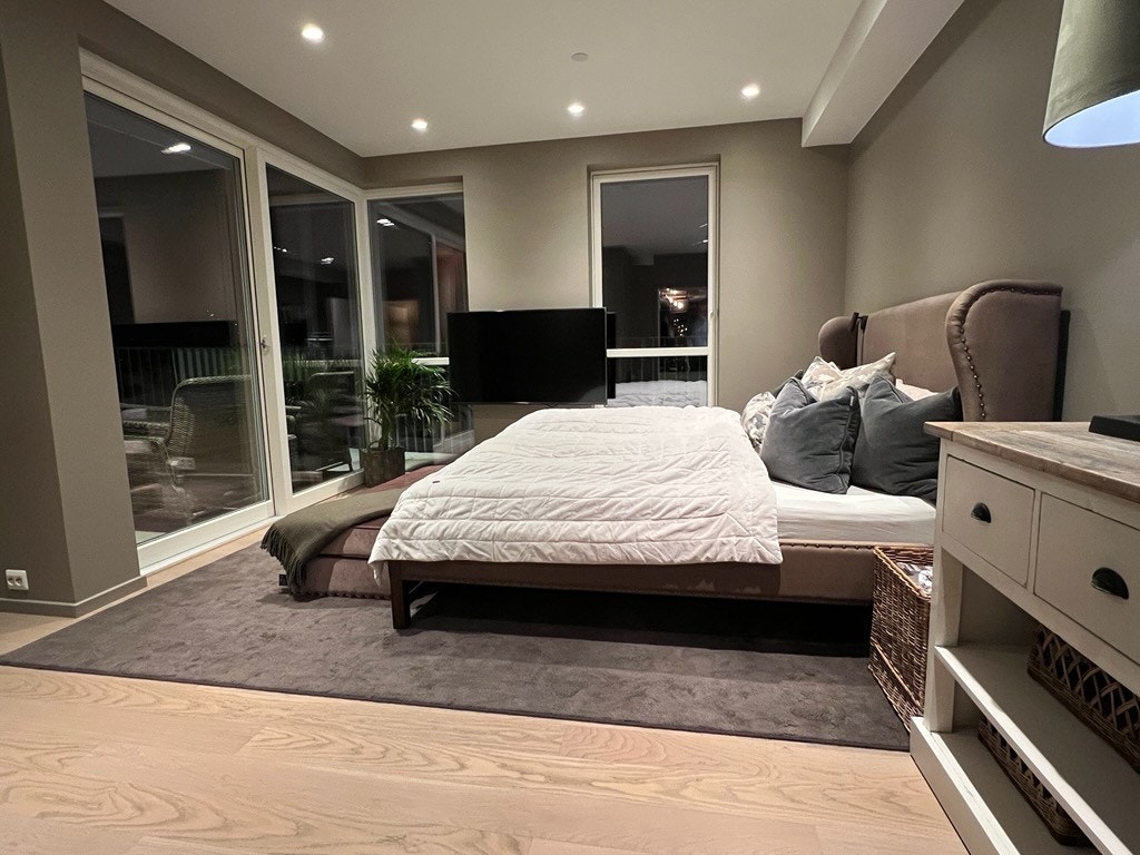 Her er det god plass til en romslig dobbeltseng, og de takhøye vinduene gir rommet en ekstraordinær kvalitetsopplevelse. Med TV på veggen kan du slappe av og nyte en god film, mens den generøse gulvplassen skaper en luftig og behagelig atmosfære. Galleribilde