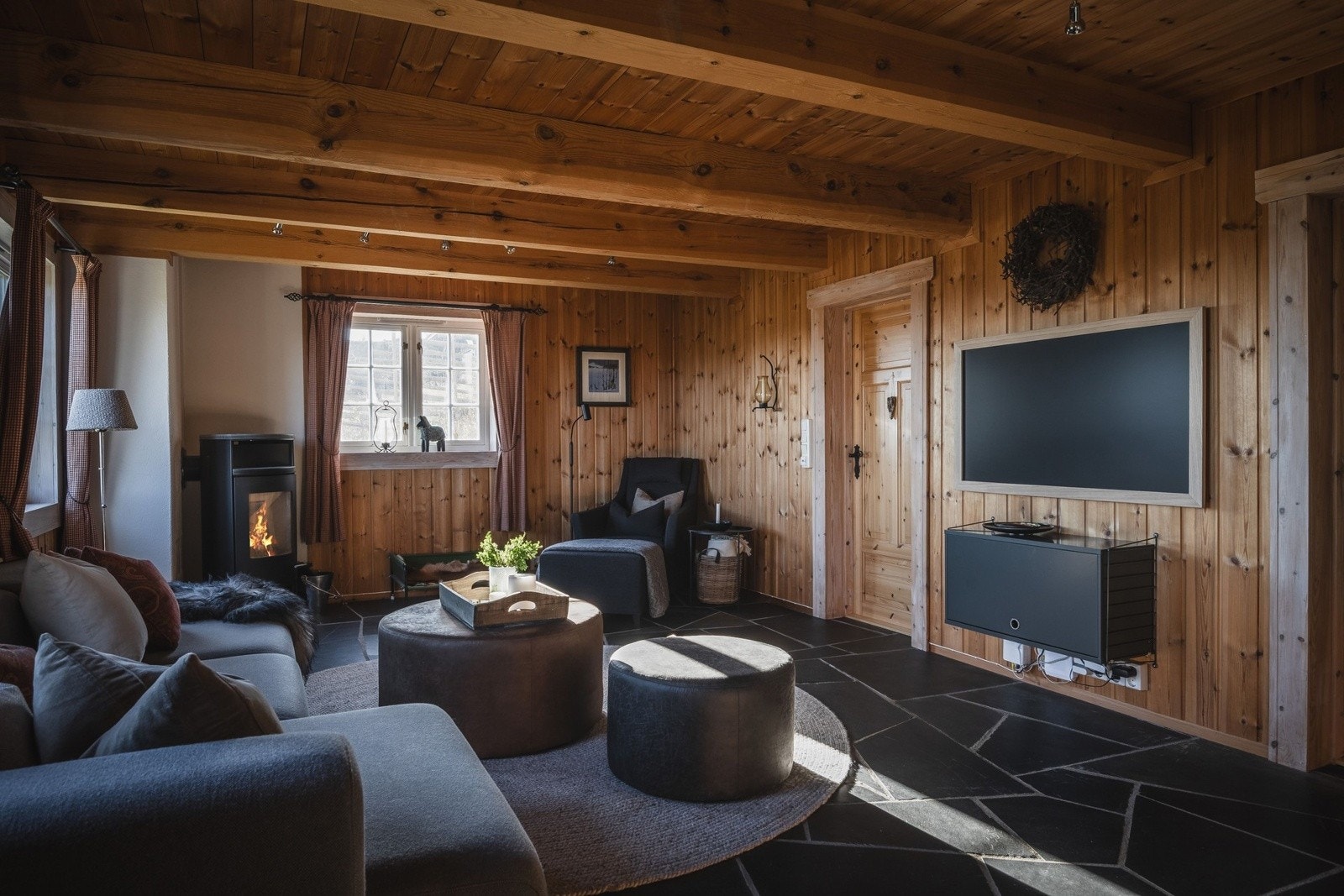 Lun og trivelig TV-stue med plass til stor sofa og koselige sittegrupper. Rommet inviterer til avslapning og underholdning, enten det er filmkvelder med familien eller rolige stunder med en bok. Fra tv-stuen er det inngang til bad og vaskerom. Galleribilde