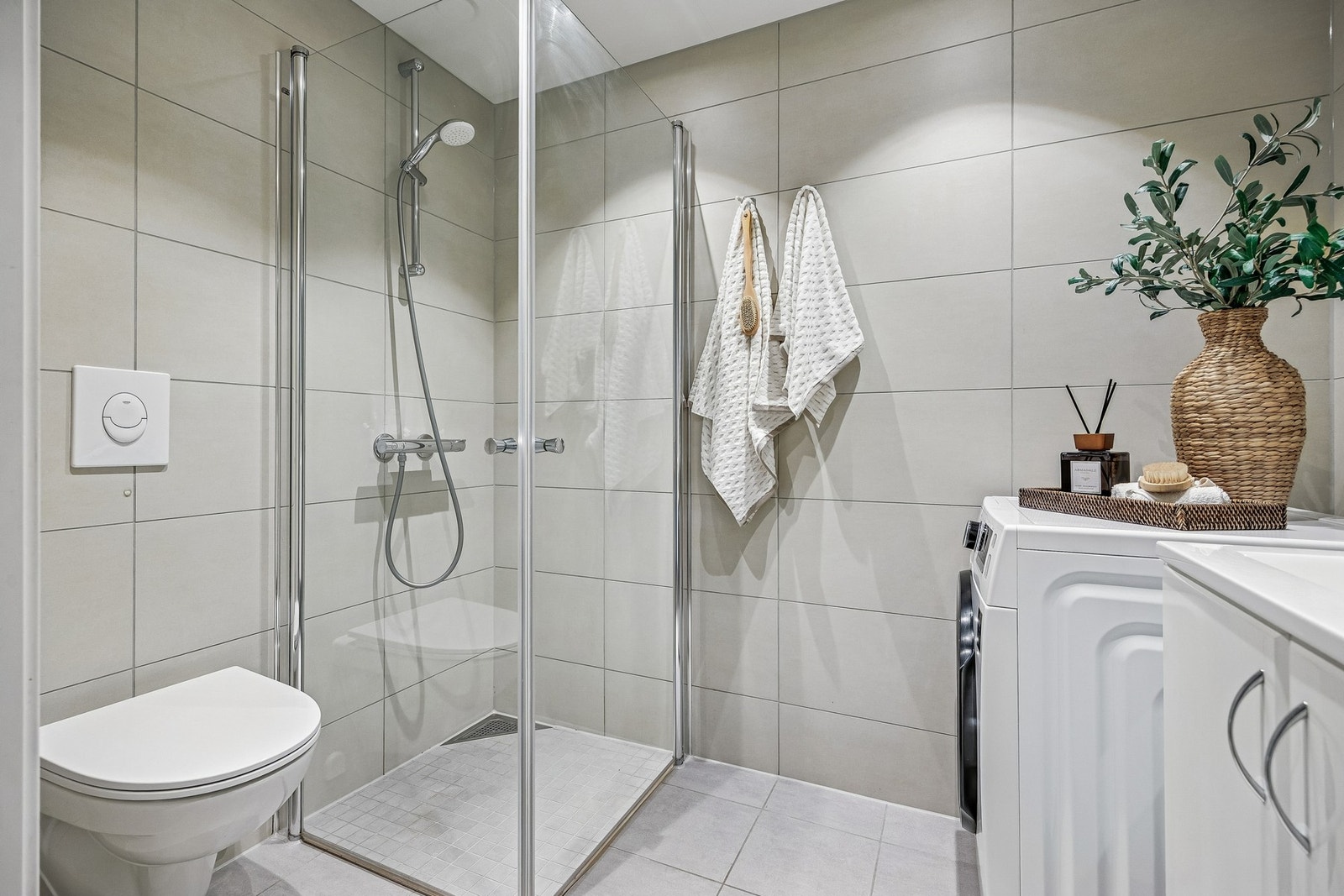 Det er utstyrt med innfellbare dusjdører, servant med skap, veggmontert wc, mekanisk avtrekk og opplegg for vaskemaskin - alt samlet i en funksjonell og stilren løsning som gir høy komfort i hverdagen. Galleribilde