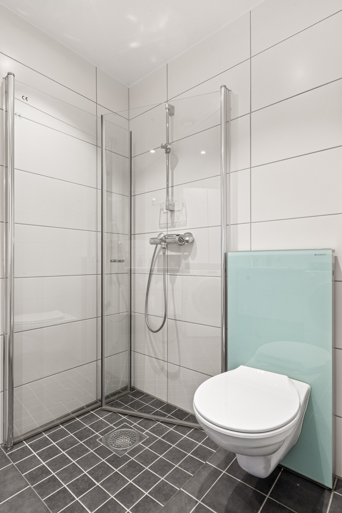 Badet er innredet med nedfelt servant, veggfestet toalett, dusjhjørne og opplegg for vaskemaskin. Galleribilde