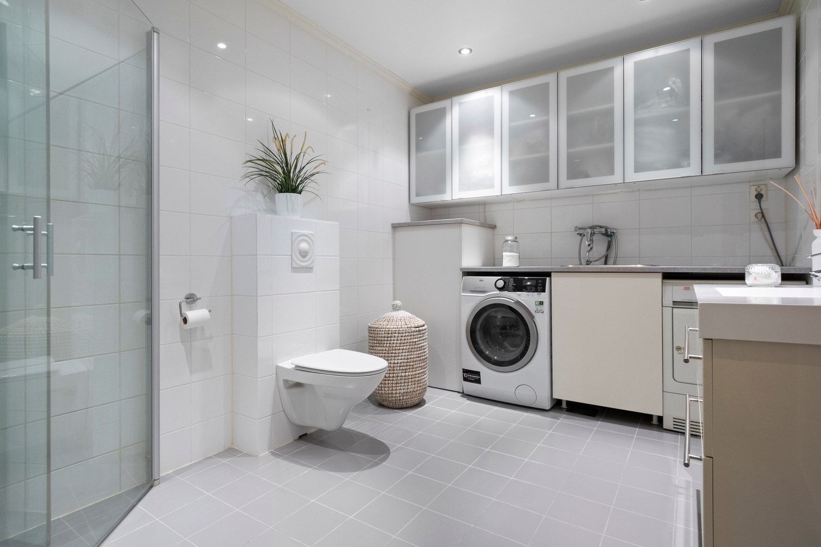 Bad/vaskerom har flislagte vegger og flislagt gulv med varmekabler, samt innredning med servant, veggmontert toalett og dusjdører. Galleribilde