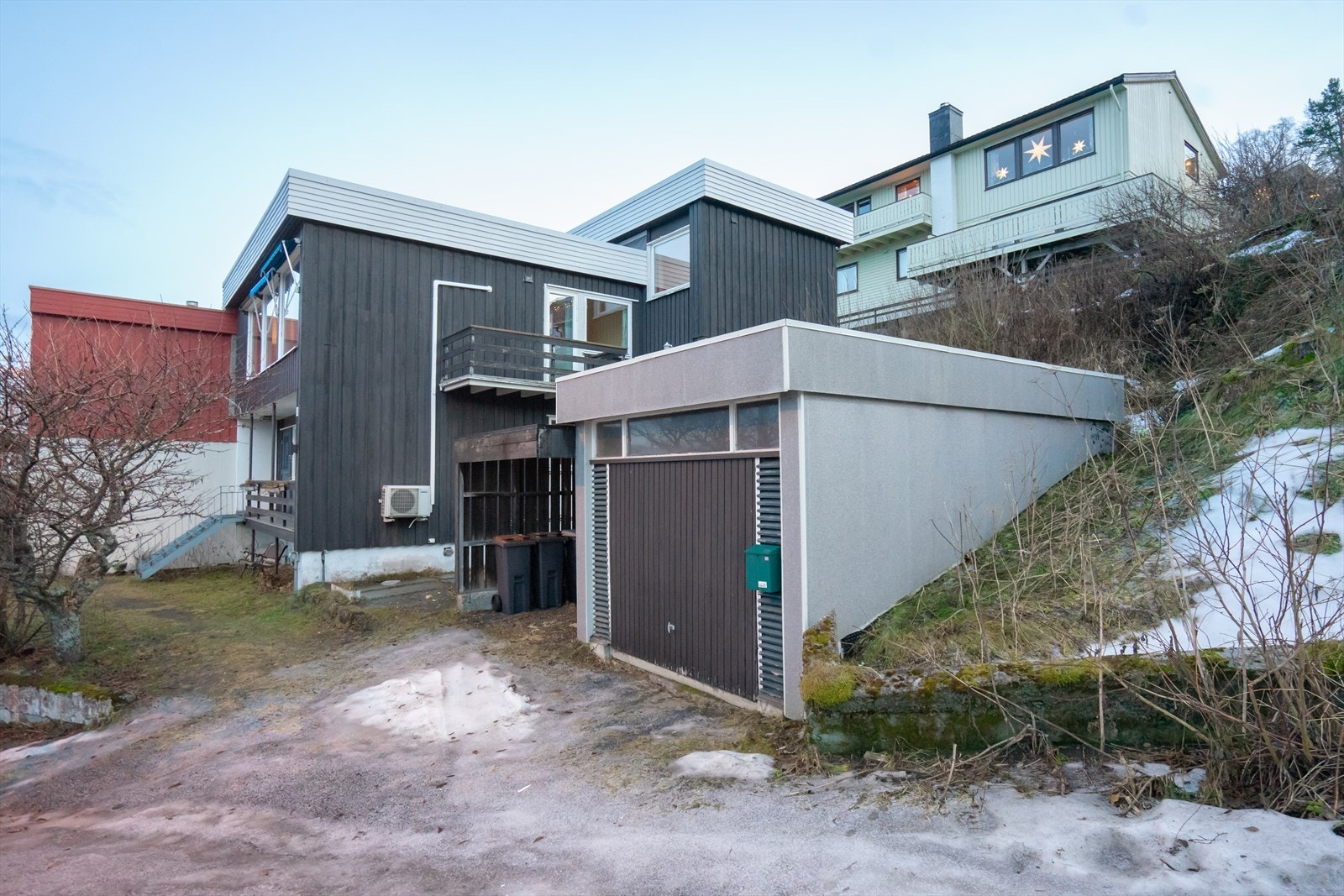 Frittstående garasje med tilhørende liten carport. Gulv i garasje er utført som grovstøpt betongplate. Galleribilde