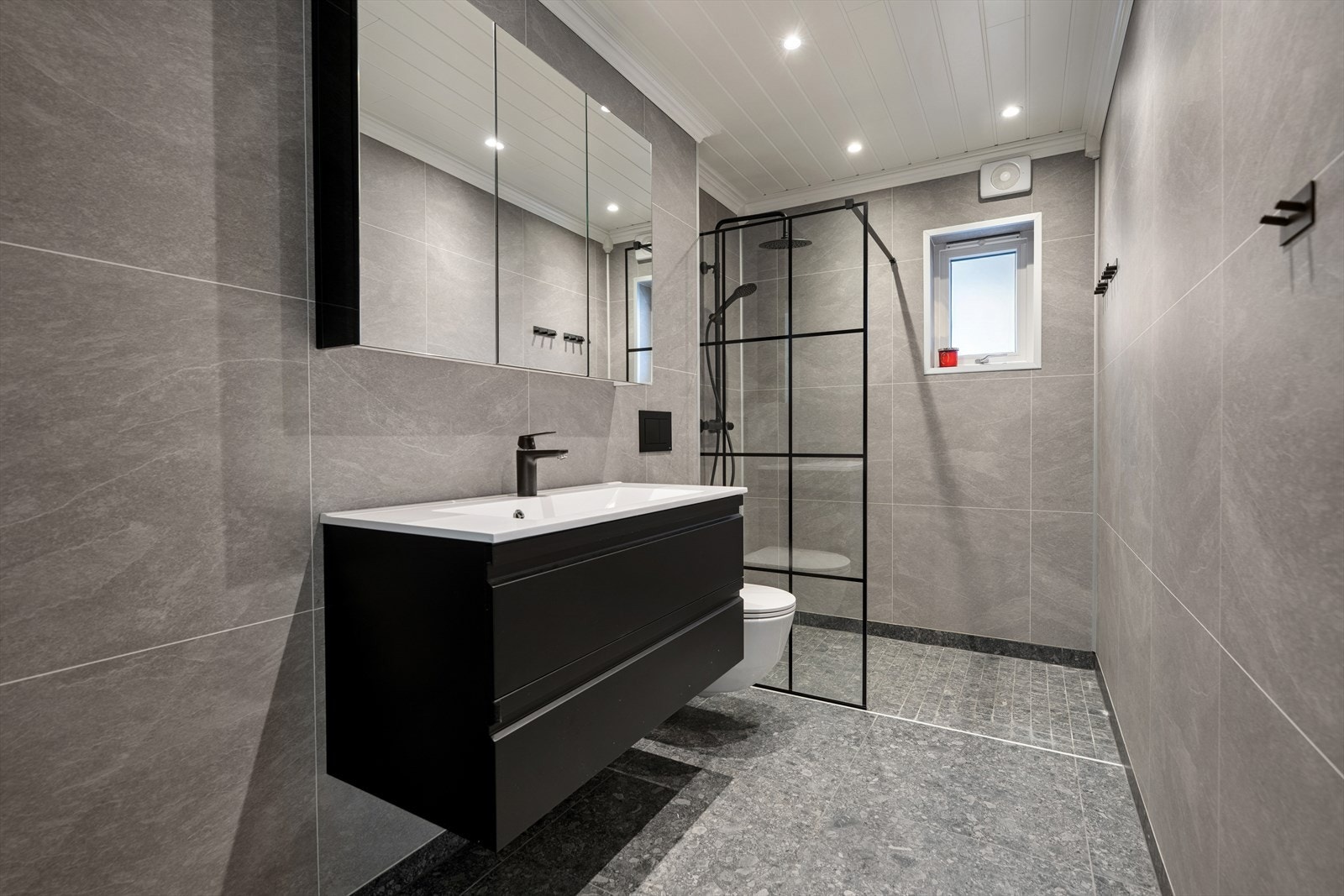 Baderommet fremstår som pent og funksjonelt, med baderomsplater på veggene som gir et rent og moderne uttrykk. Gulvet er belagt med fliser og komfortabel gulvvarme, noe som gir en behagelig opplevelse, særlig på kalde dager. Galleribilde