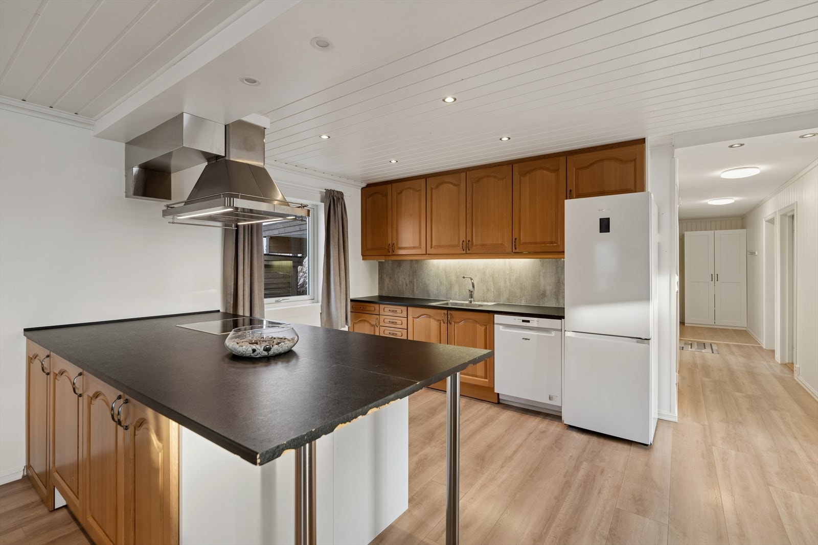 Kjøkkenet i første etasje fremstår som et lyst og praktisk innredet rom med laminatgulv, malte slette veggflater og panel med downlights i himlingen, noe som skaper en varm og innbydende atmosfære. Galleribilde