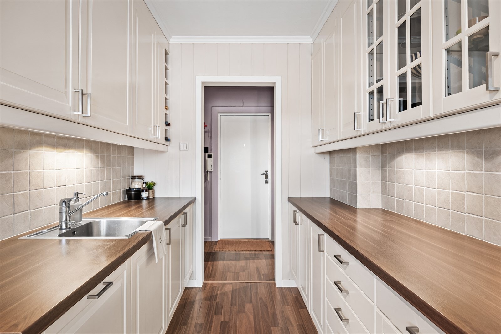 Kjøkkenet har rikelig med skap- og benkeplass på begge sider. Flotte detaljer med vitrineskap, vinhylle, veggfliser og ekstra lys over benk. Alle hvitevarer er integrerte. Galleribilde