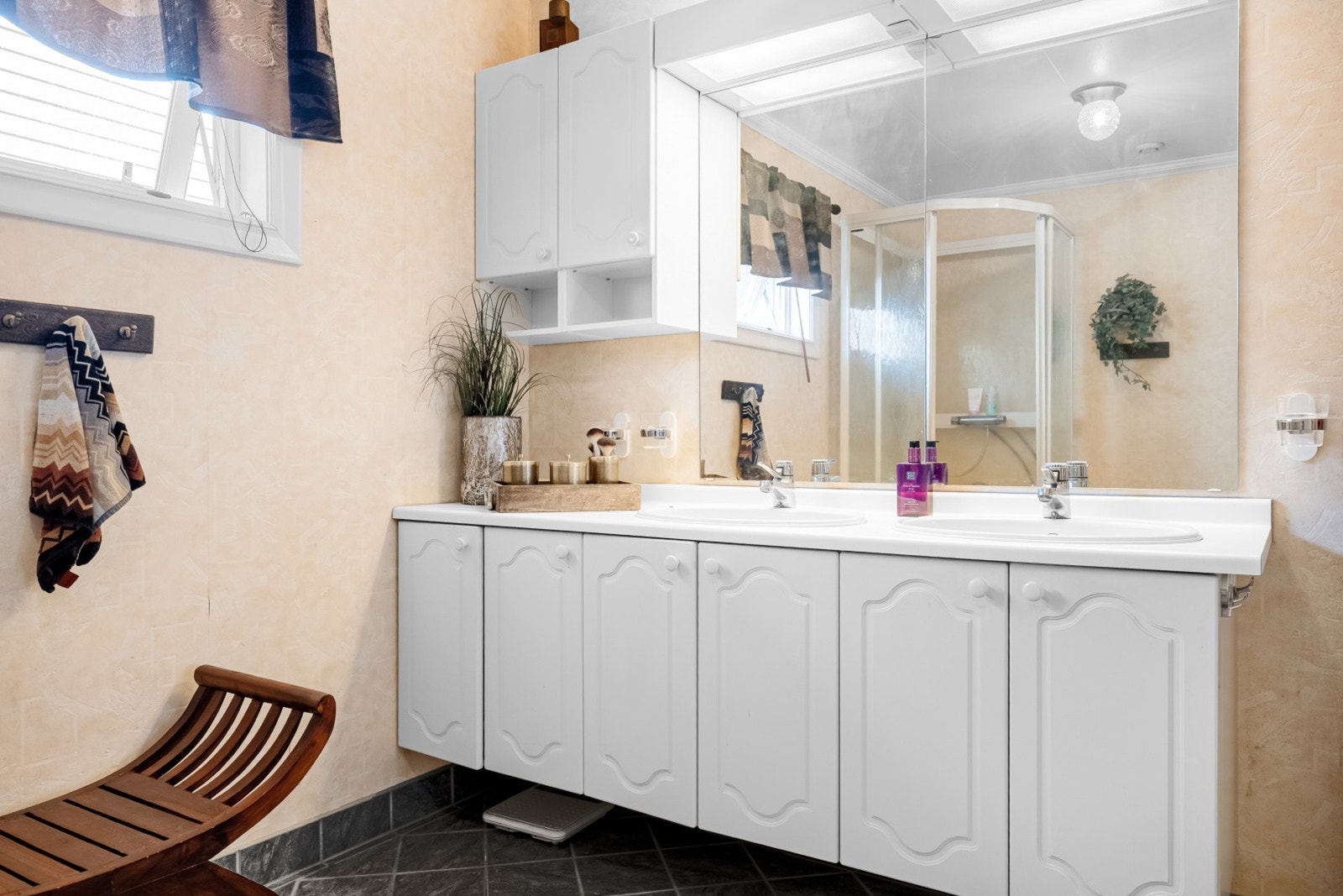 Badet har benkeinnredning med to nedfelte servanter, dusjkabinett, gulvmontert toalett og en bidét. Galleribilde