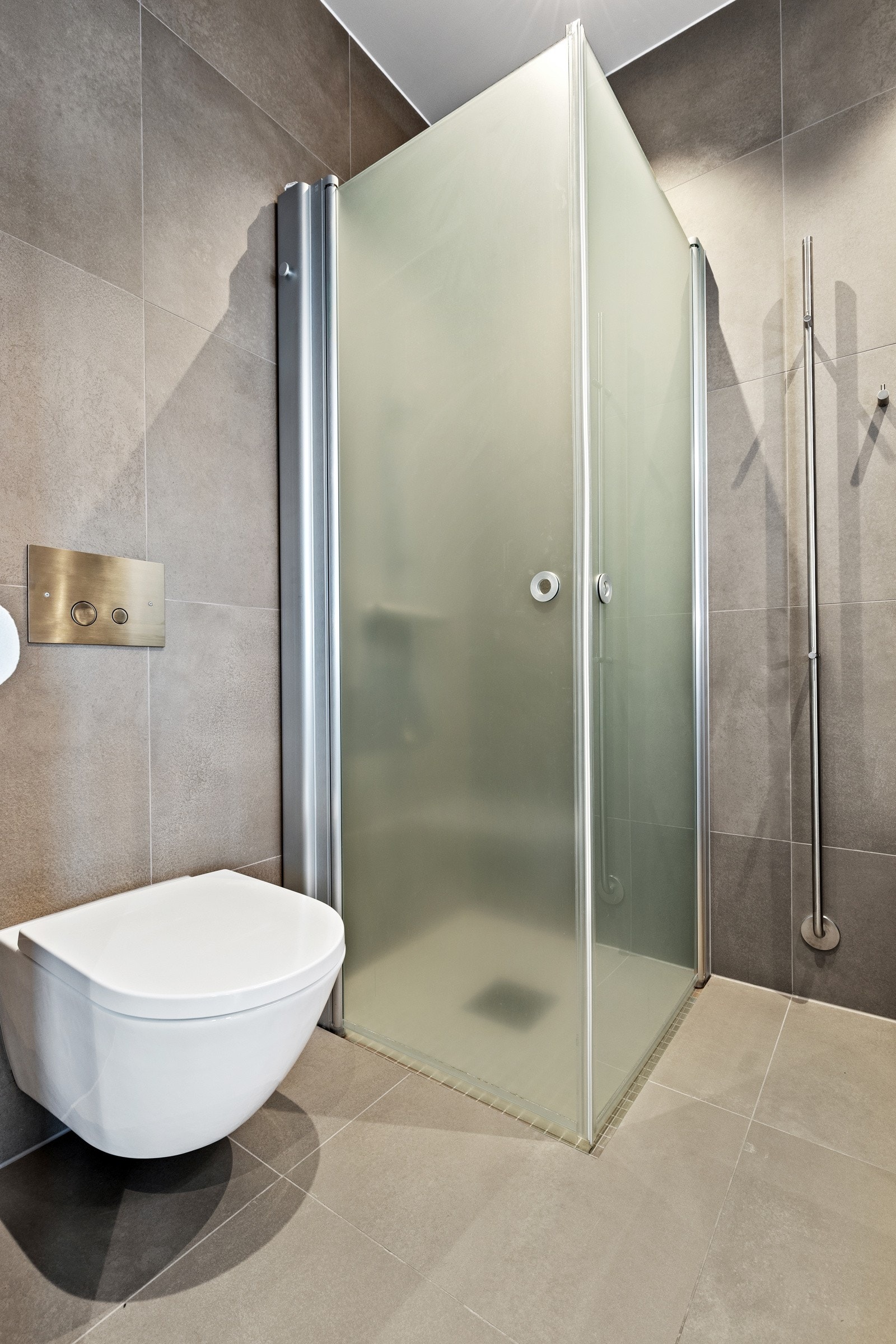 Separat dusjhjørne med mindre fliser på gulv, innfellbare glassdører og hånddusj. Himlingen er lyssatt med downlights. Galleribilde