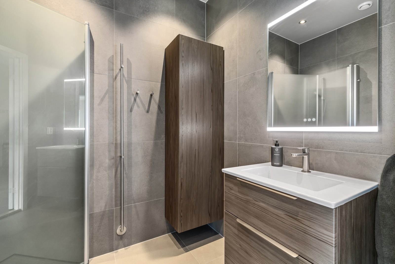 Delikat flislagt bad m/gulvvarme i boligens 1. etasje. Innredningen består av stilrent servantmøblement med 2 skuffer, speil, tilhørende høyskap og vegghengt toalett. Galleribilde