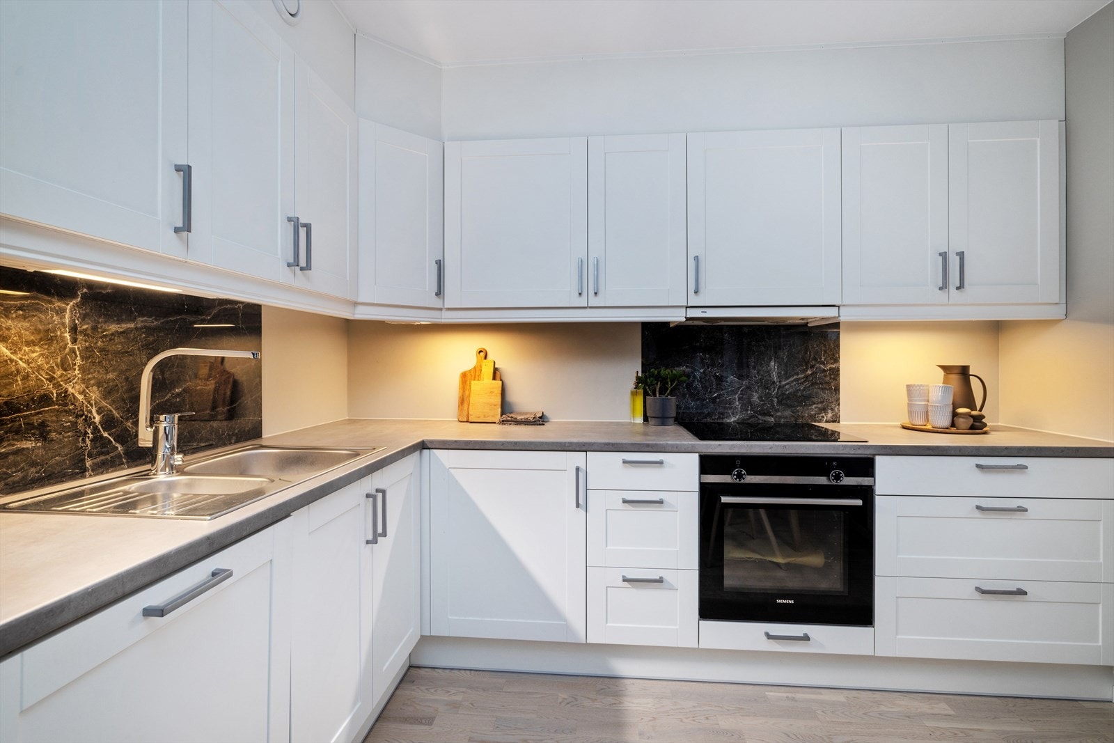 Hvitt kjøkken med profilerte fronter og laminat benkeplate. Kjøkkenet er utstyrt med hvitevarer som kjøl/fryseskap, oppvaskmaskin, induksjonstopp, stekeovn, vannstoppsystem og komfyrvakt. Galleribilde