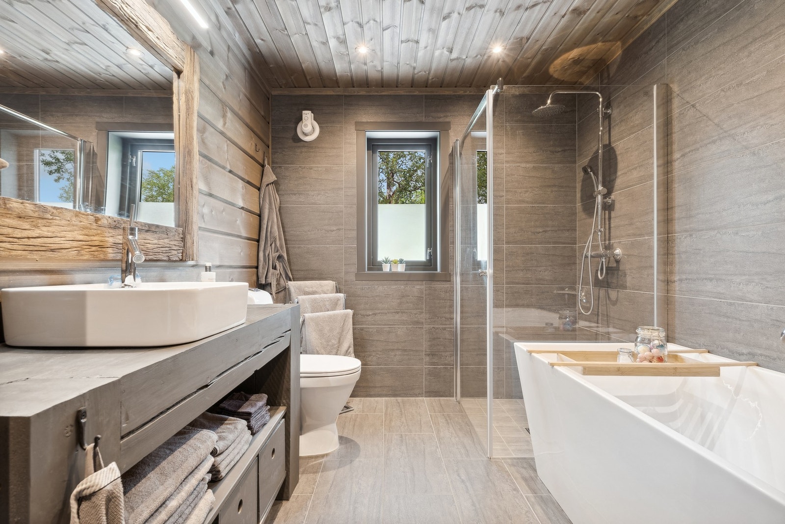 Badet er på 6 kvm og har flis på gulv samt flis/panel på vegger. Inneholder toalett, dusjhjørne med glassvegger, badekar og toppmontert vask på plassbygd innredning. Galleribilde