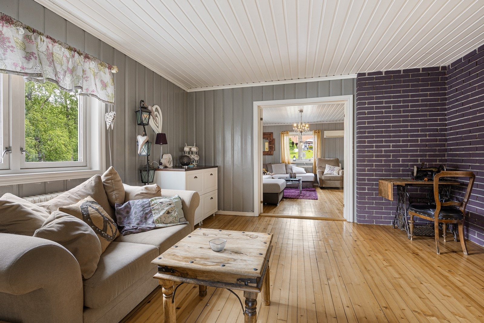 En dobbel glassdør skiller stuene, og begge rommene er innredet med tregulv og panelvegger malt i grått. Galleribilde