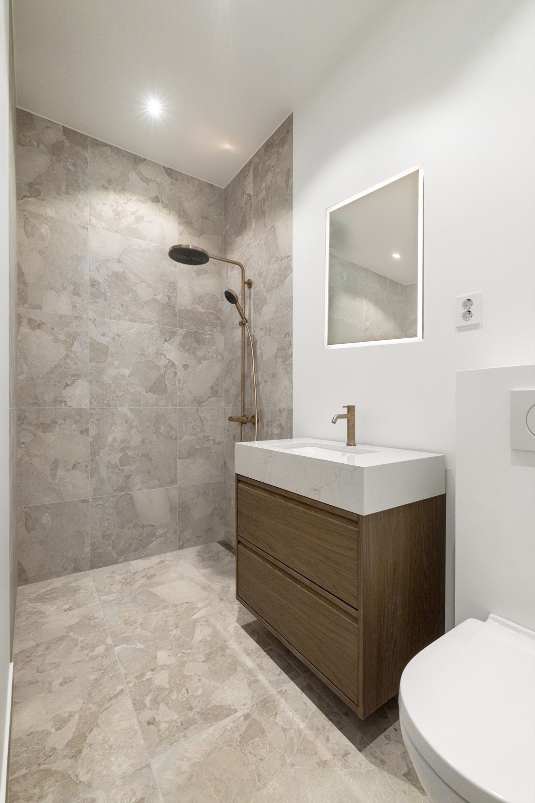 Bad 2 fra 2025 med vegghengt toalett, servant med skuffer og romslig dusjnisje med glassdør. Galleribilde