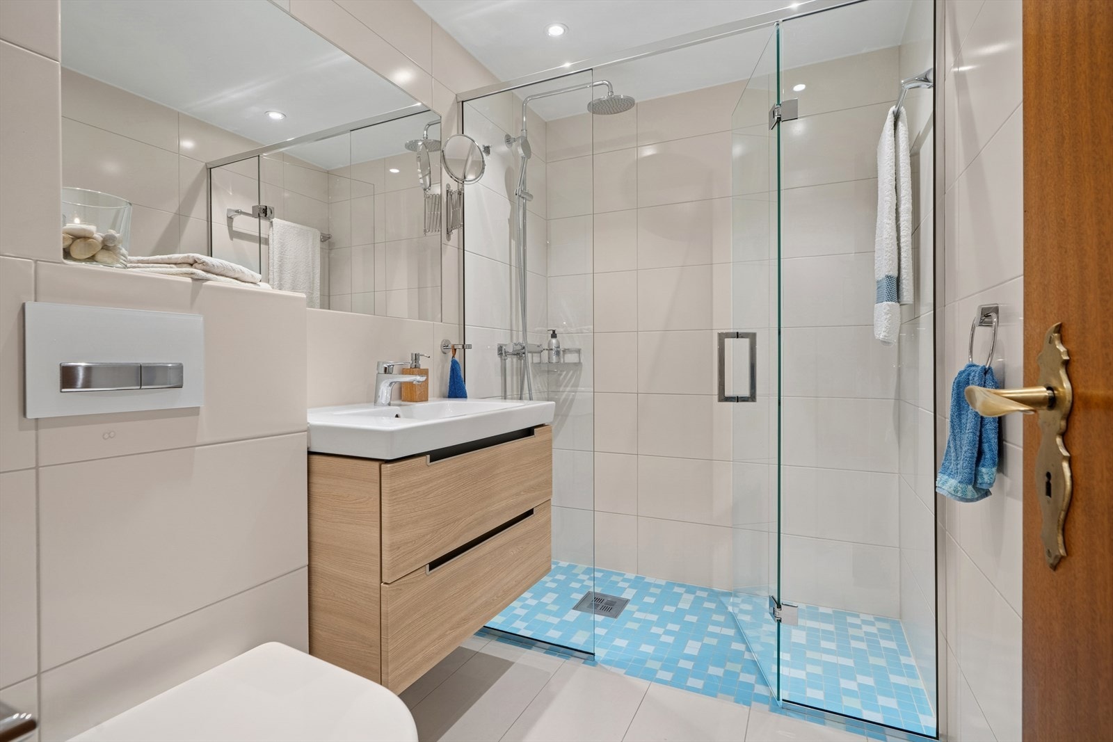 Hovedbaderom innredet med vegghengt klosett, servantinnredning, innfelt speil og dusjhjørne med svingbar glassdør. Galleribilde