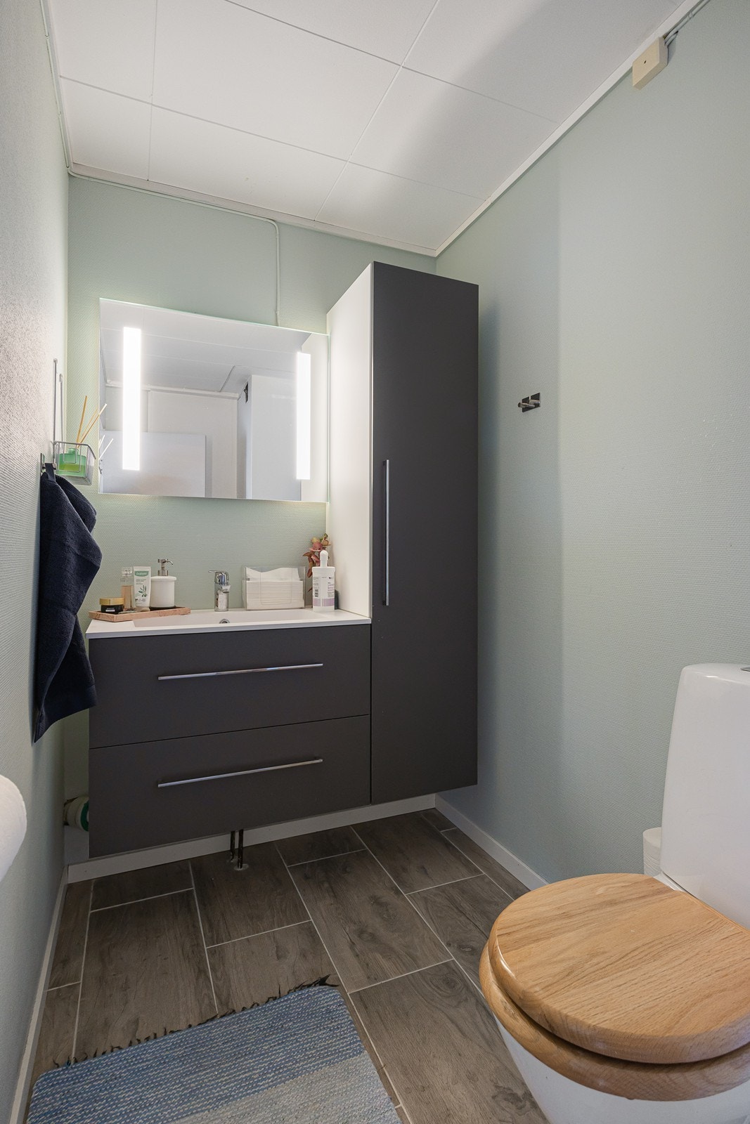 I praktisk tilknytning til entréen ligger dette wc-rommet med fliser på gulvet. Innredningen har hedekkende servant over skuffeseksjon, matchende høyskap og speil med integrert belysning. Galleribilde