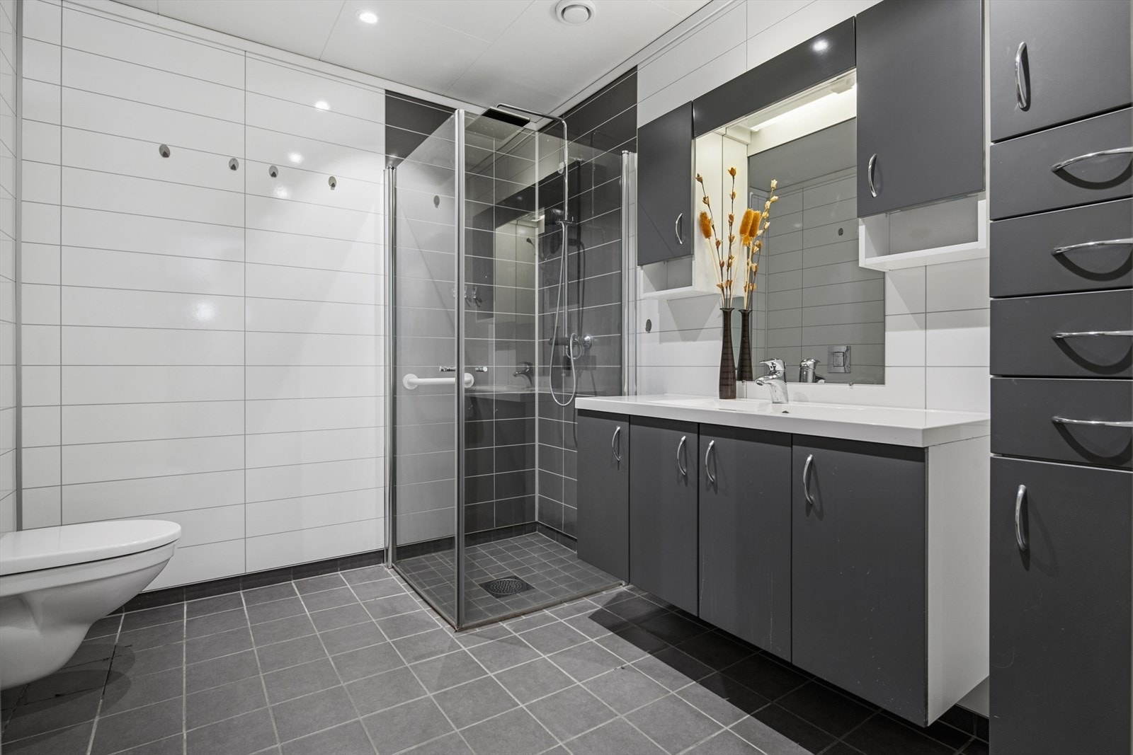 Badet har flislagt gulv med varmekabler, dusjvegger og vegghengt toalett. Galleribilde