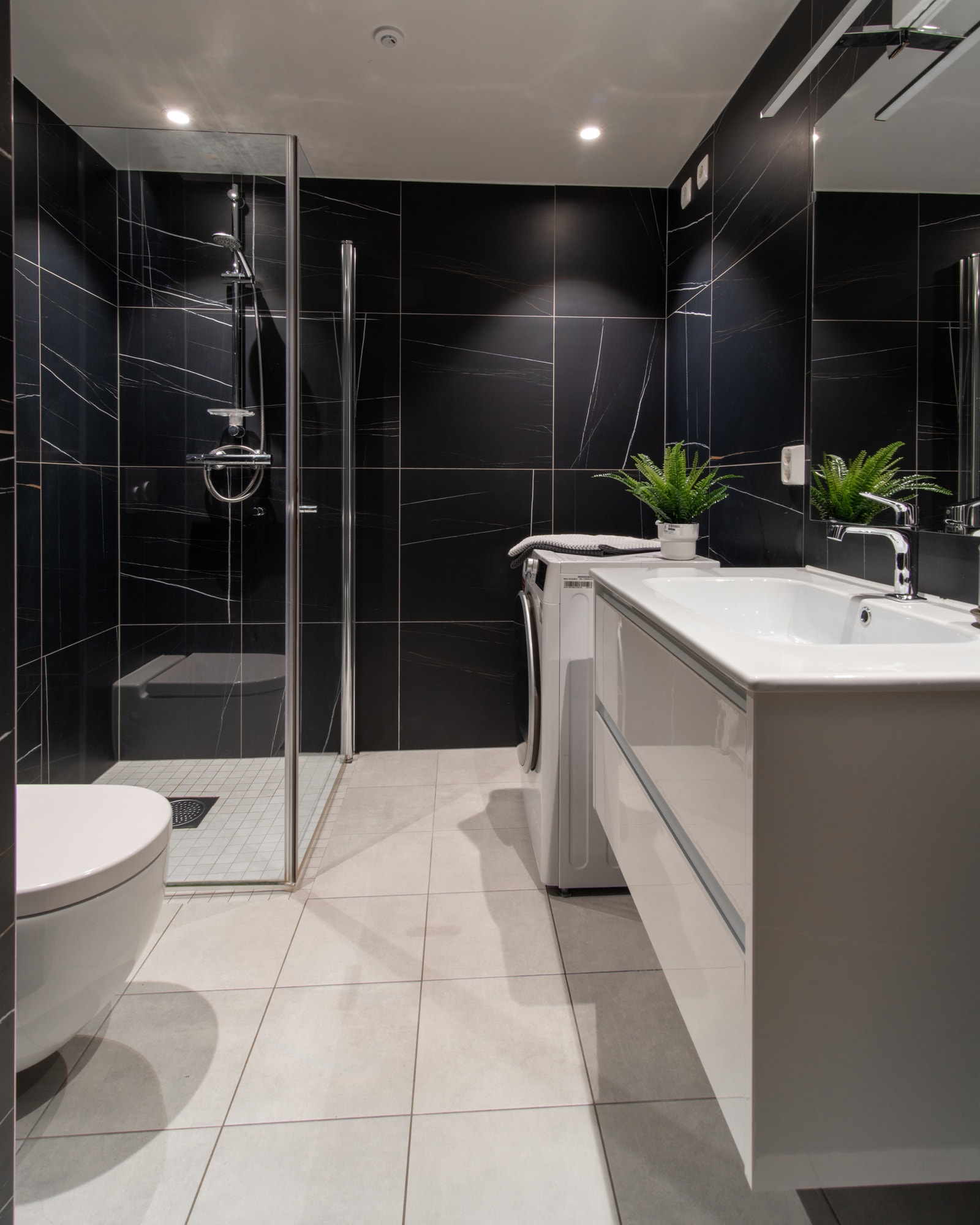 Pent flislagt bad med hjørnedusj, toalett, servant og vaskemaskin. Galleribilde