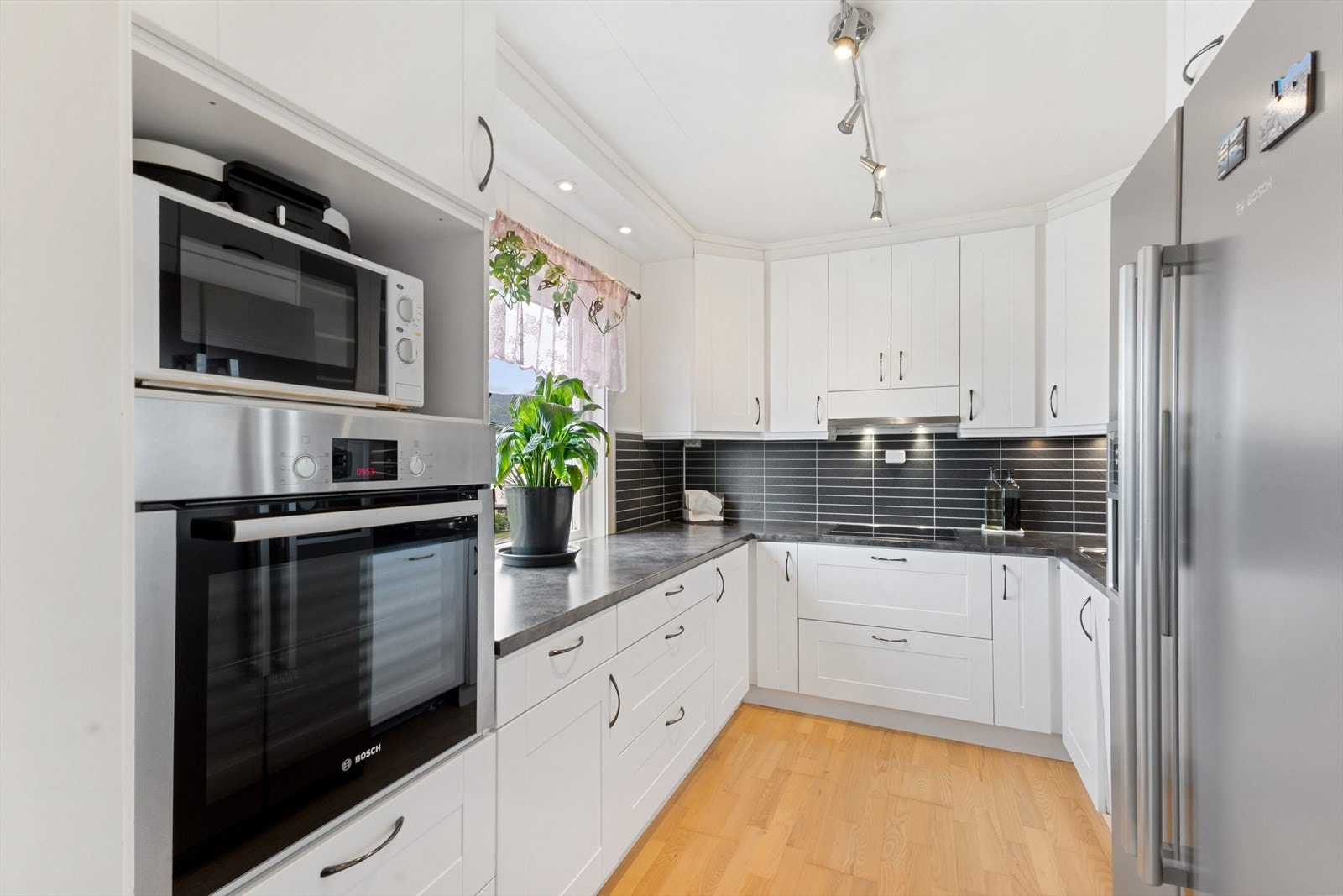 Mot kjøkkenet. Bla. Bosch stekeovn, kjøl/frys side-by-side, innfelt koketopp, downlighs over kjøkkenbenk og lysskinner i himling. Galleribilde