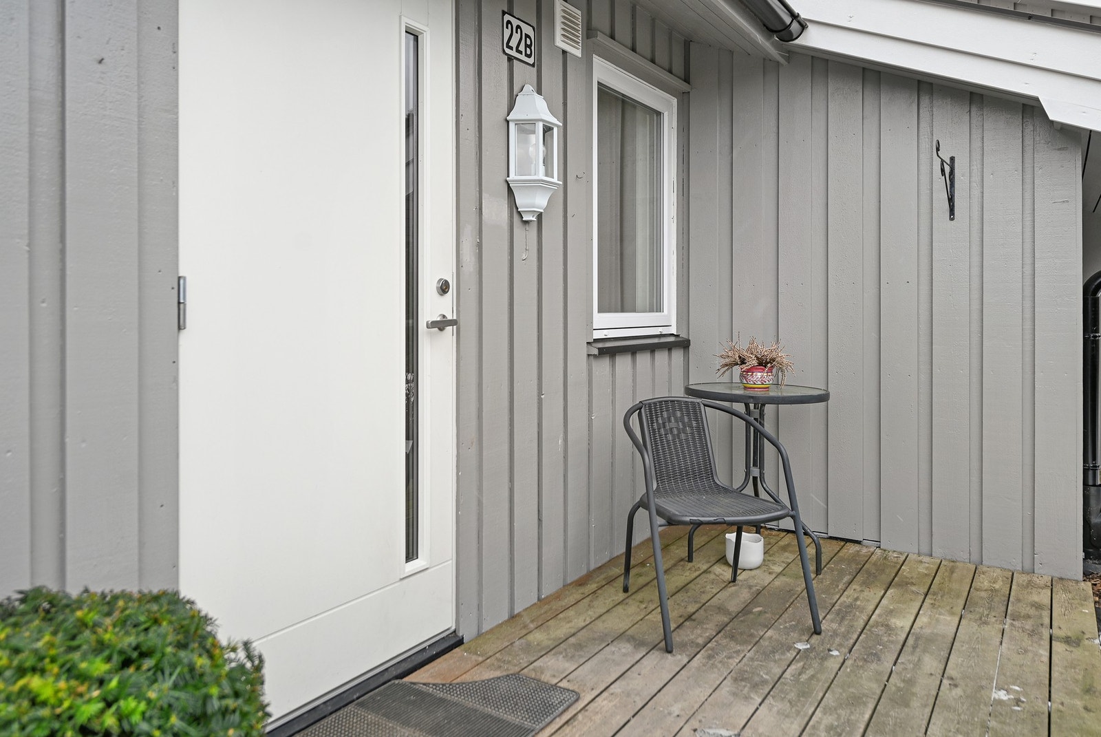 Inngangsparti med grå panelvegger og hvit dør. Liten uteplass med bord og stol. Galleribilde
