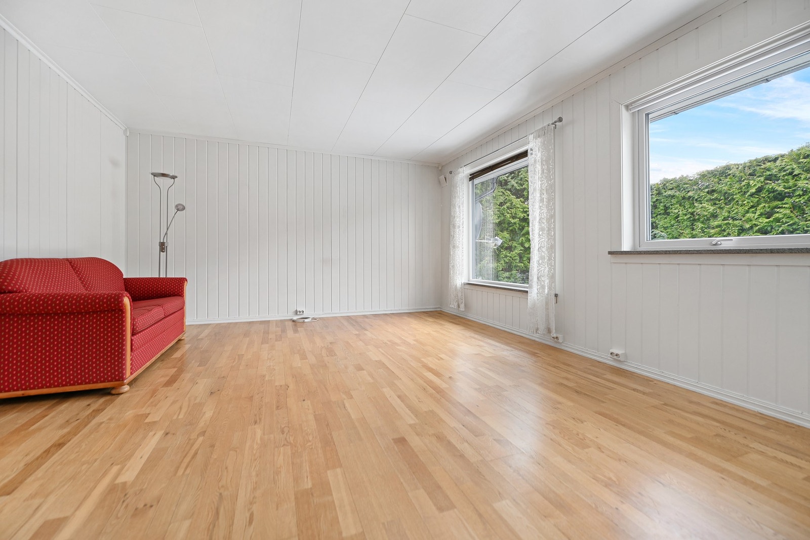 Lyst rom med vinduer som gir godt med naturlig lys. Vegger og tak er hvitmalte. Gulvet er av tre. Galleribilde