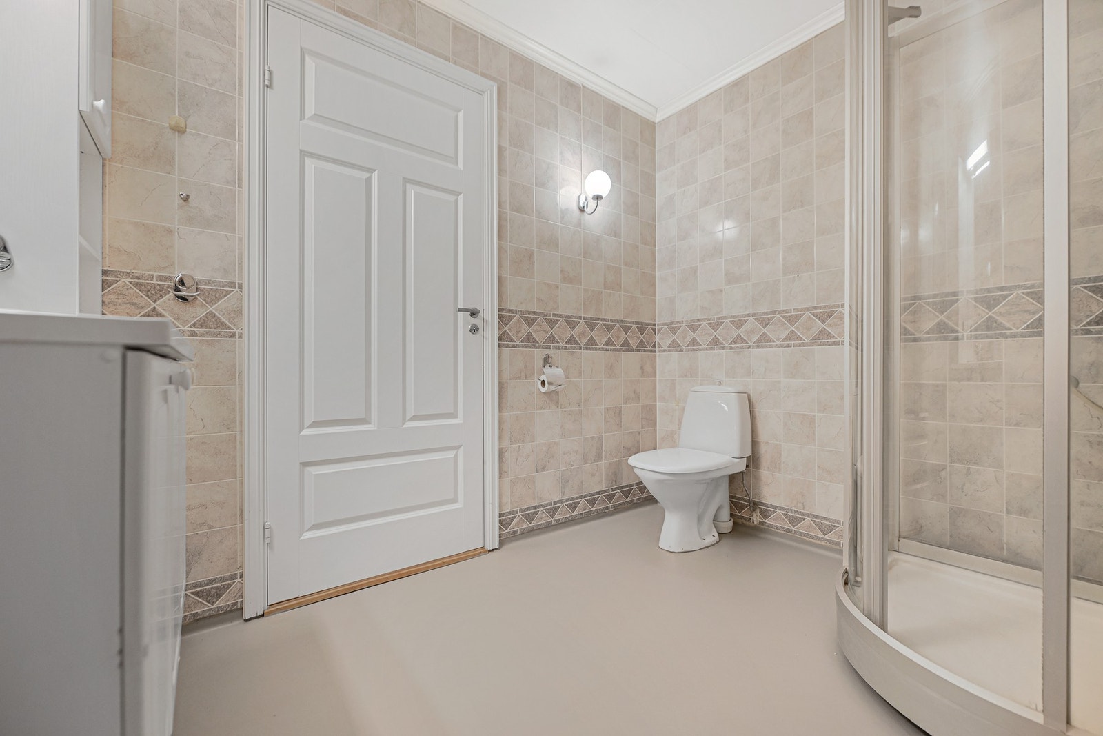 Baderom med dusjkabinett, toalett og fliser på veggene. Lys og funksjonell innredning. Galleribilde