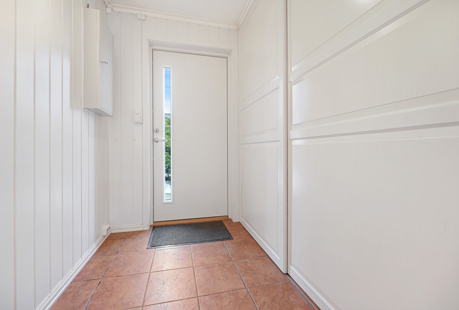 Lyst inngangsparti med flislagt gulv og hvite panelvegger. Galleribilde