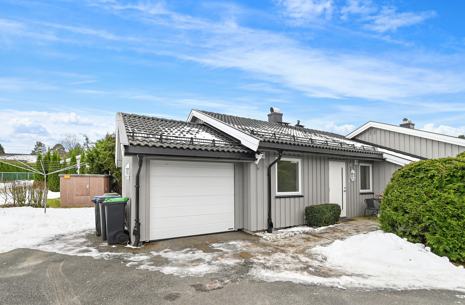 Grå enebolig med garasje, uteområde og asfaltert innkjørsel. Snø på bakken og blå himmel med skyer. Galleribilde