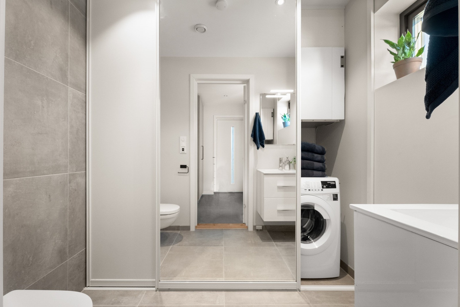 Vaskerommet har flislagt gulv med varme. Plass til både vaskemaskin og tørketrommel i nisjen med skyvedør. Rommet har vegghengt toalett, og servant med skuffer. Galleribilde