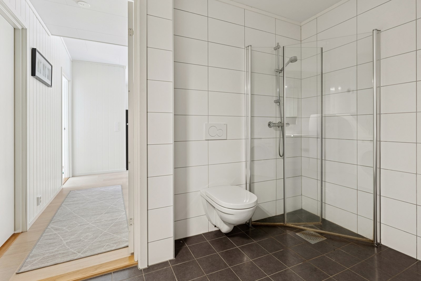 Baderommet har et eget dusjhjørne og et veggmontert toalett. Galleribilde
