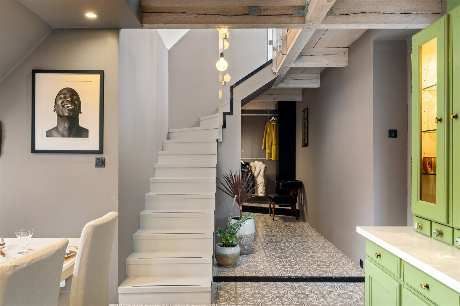 Videre inn i gangen knyttes etasjene sammen med kjøkken og stue i en harmonisk helhet. Her møter rustikke detaljer moderne linjer og belysning, noe som skaper et tøft og gjennomført arkitektonisk uttrykk. Galleribilde