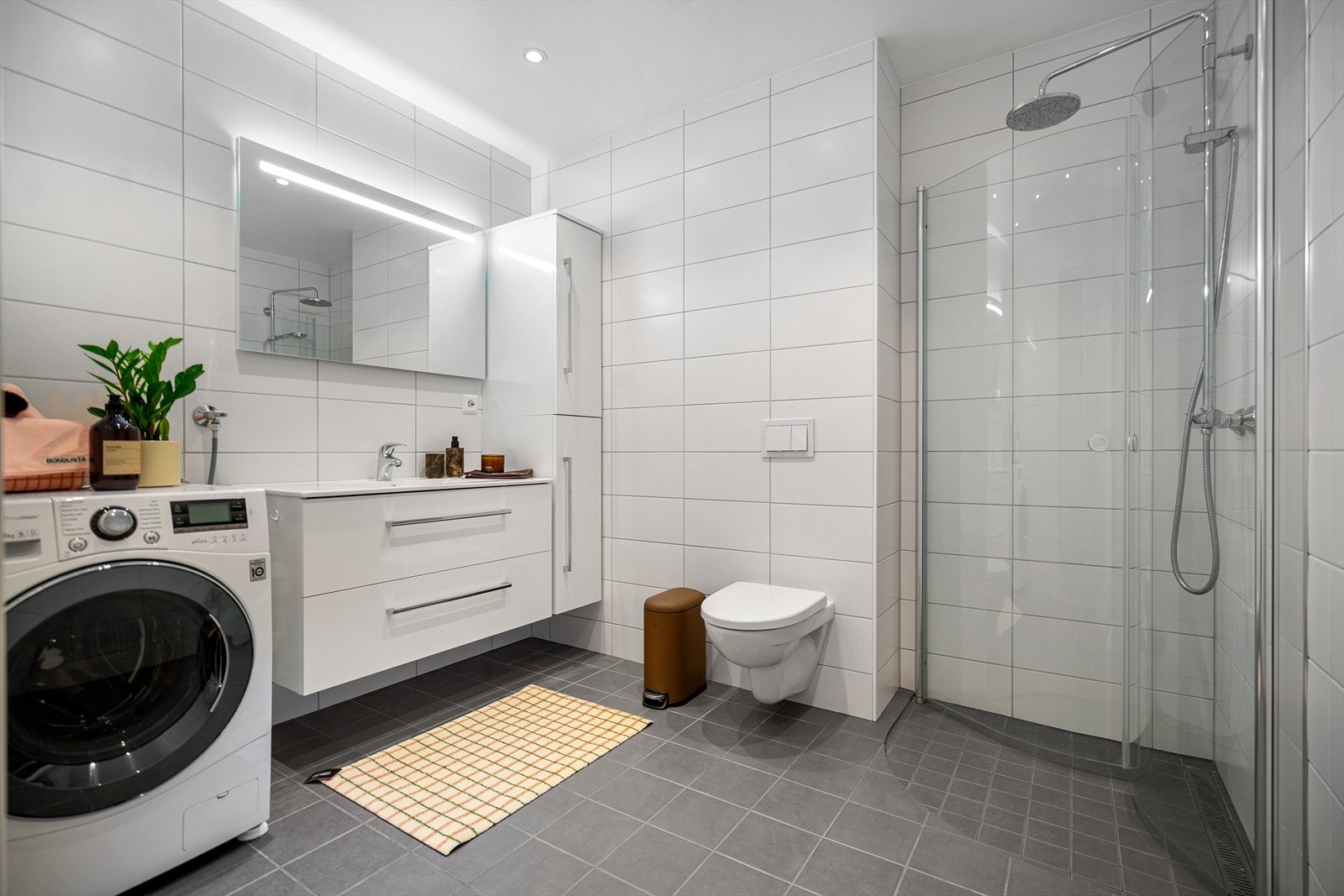 Badet har innredning med nedfelt servant, veggmontert toalett, dusjvegger og opplegg for vaskemaskin. Galleribilde