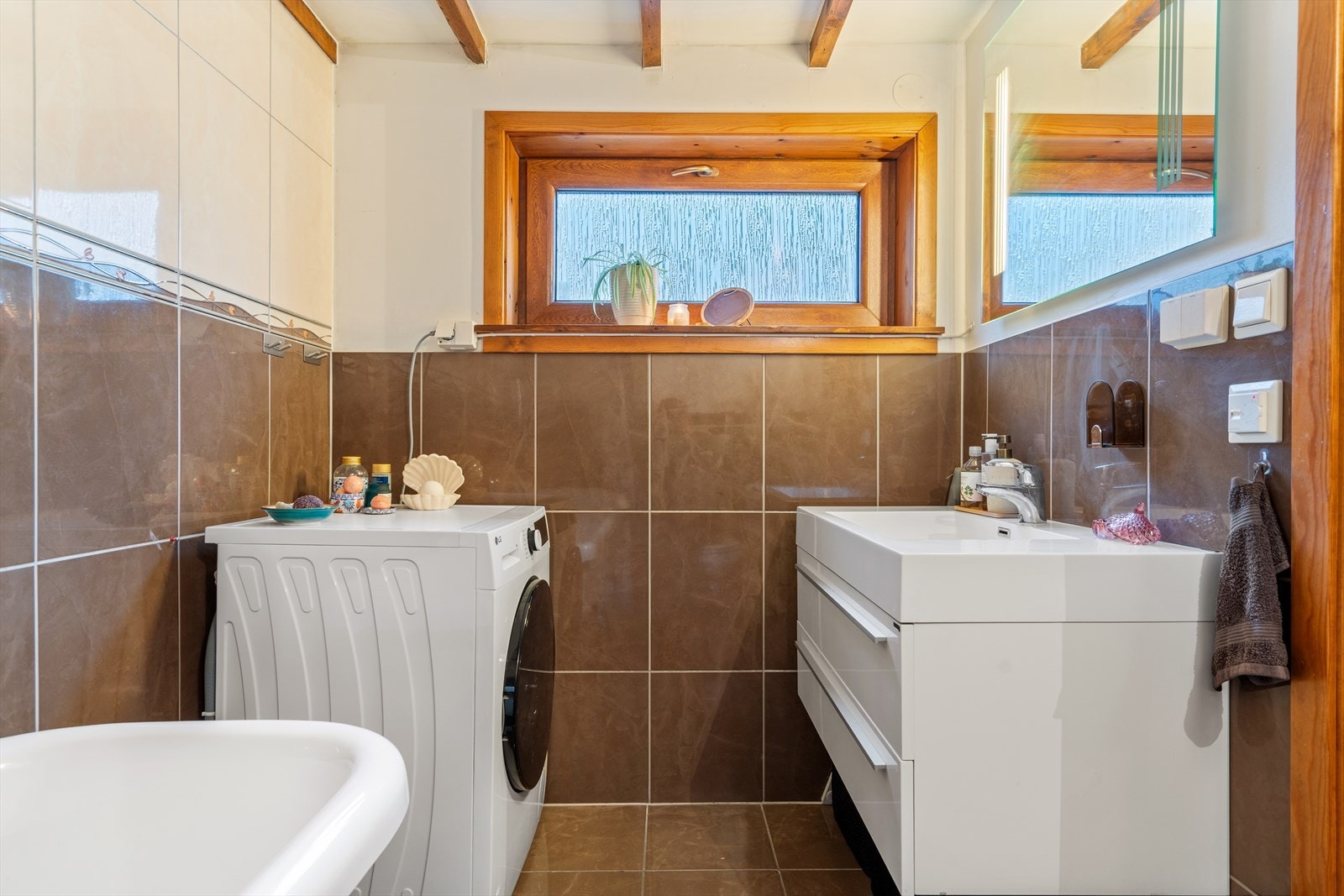 Bad/vaskerom i kjeller med flislagte vegger og gulv. Rommet har elektriske varmekabler. Innredning med nedfelt servant, veggmontert toalett og badekar. Det er opplegg for vaskemaskin og tørketrommel. Det er ingen ventilering. Galleribilde