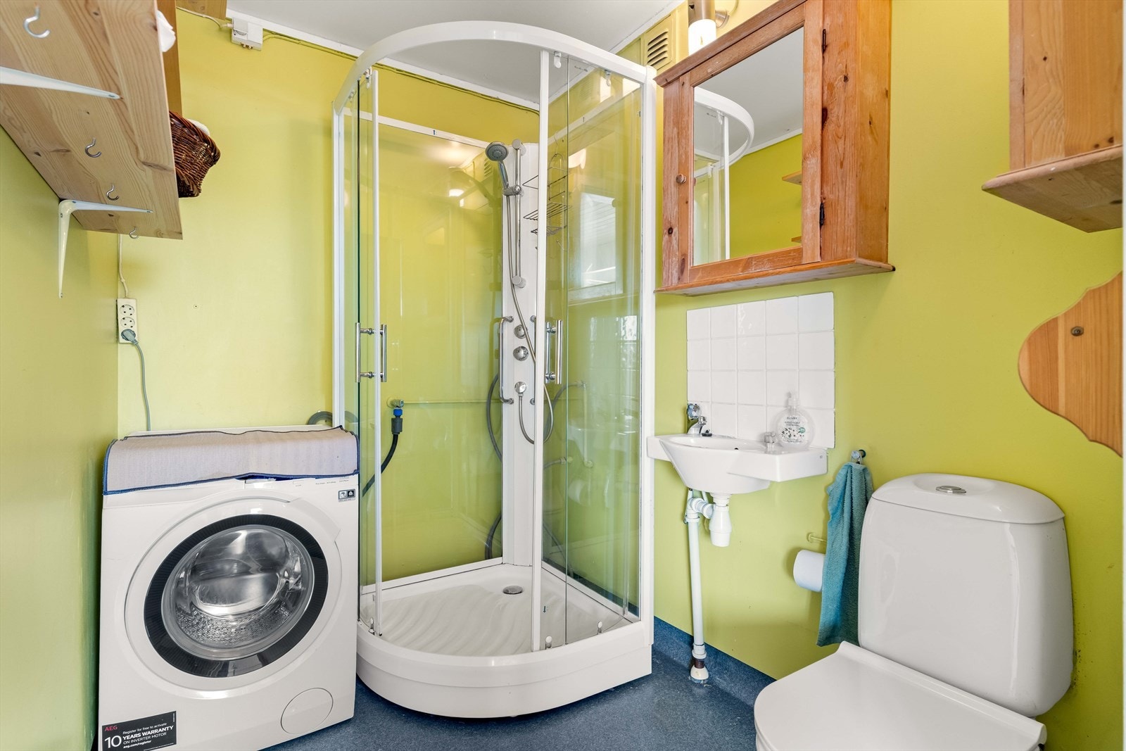 Vaskerom i 2. etasje med malte vegger og vinylbelegg på gulv. Vaskerommet har servant og 1-greps blandebatteri, speilskap på vegg, dusjkabinett, gulvstående toalett og opplegg for vaskemaskin. Galleribilde