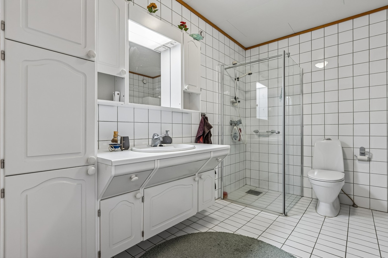 Badet har servantinnredning med profilerte fronter. Laminert benkeplate med nedfelt servantskål og 1-greps blandebatteri samt speil, overskap, overlys og høyskap. Galleribilde