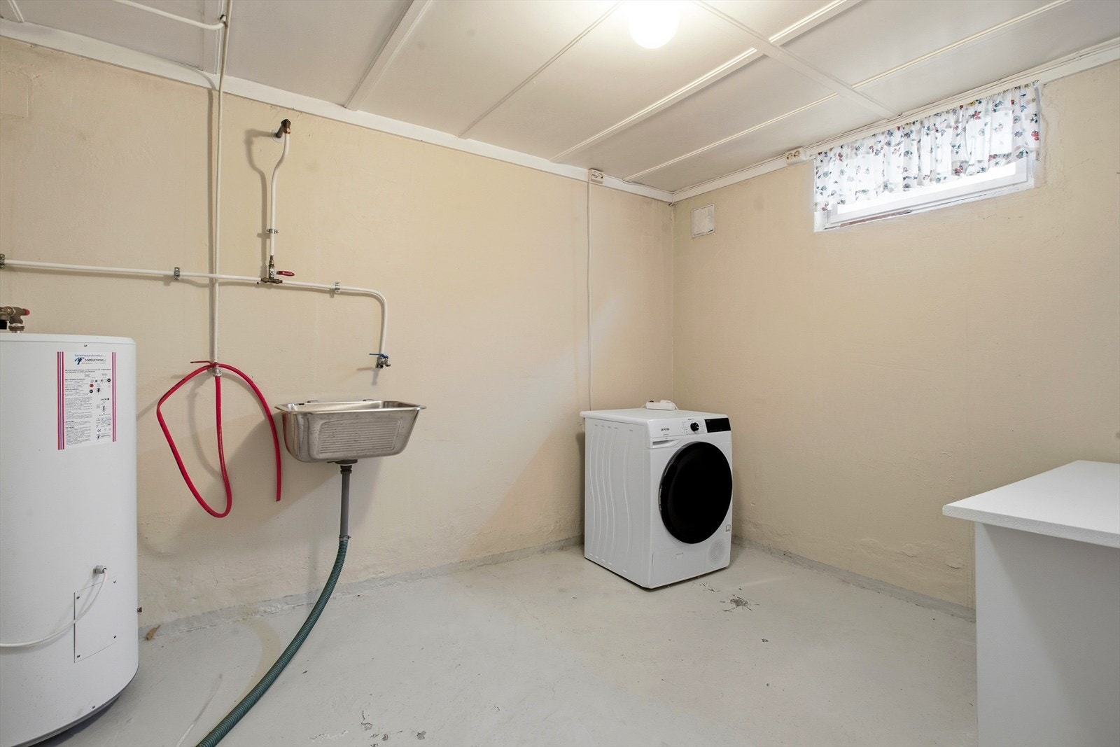 Praktisk vaskekjeller med utslagsvask, opplegg for vaskemaskin og varmtvannsbereder. Galleribilde