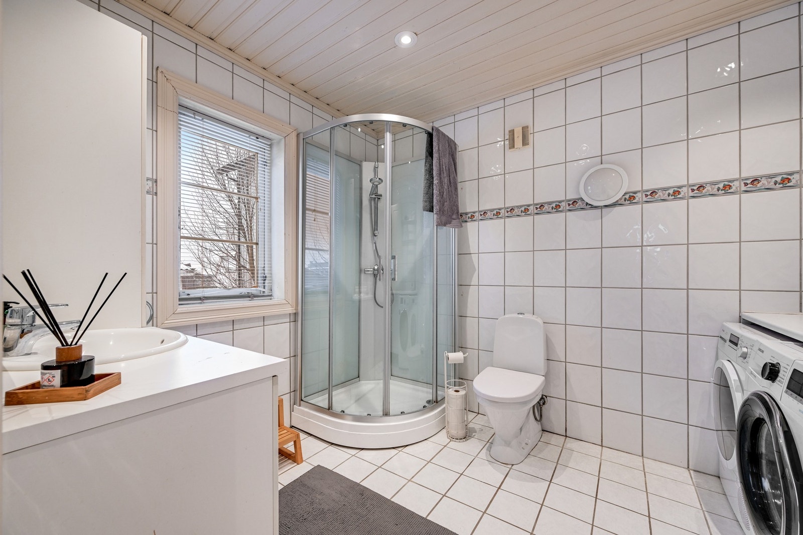 Rommet er stort og har flis på både gulv og vegger. Innredningen består av dusjkabinett, klosett, servant i innredning med underskap, og ytterligere skap for oppbevaring Galleribilde