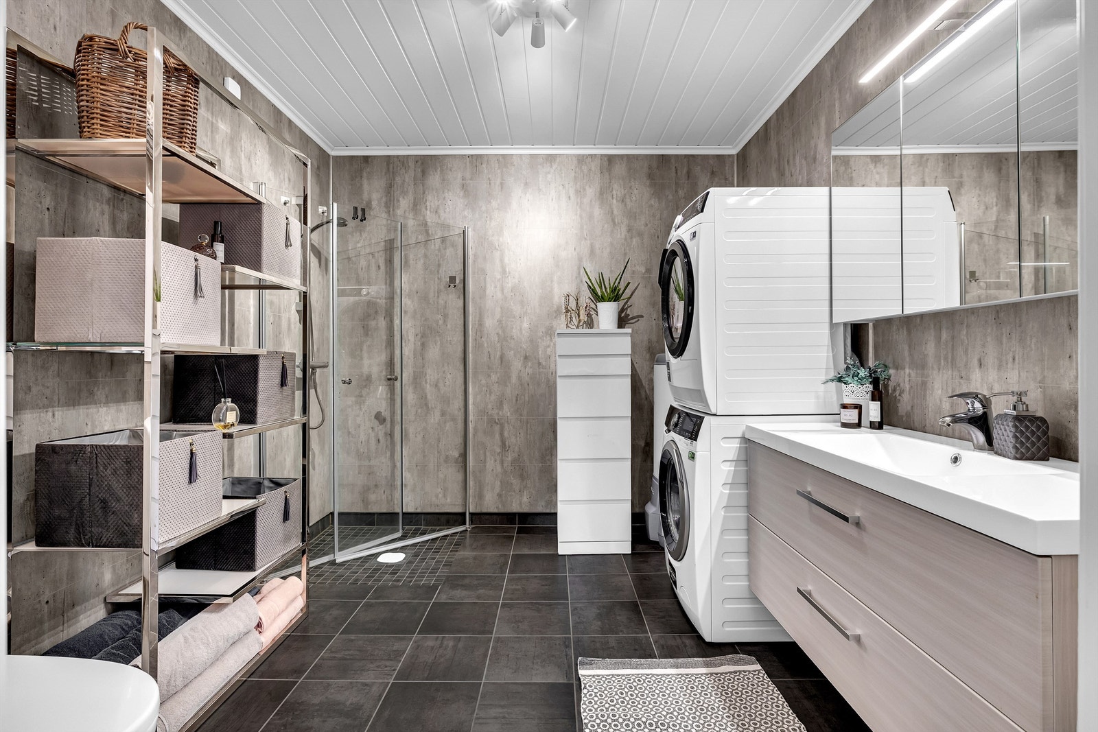 Baderommet fremstår som romslig og pent med grå fliser på gulv med gulvvarme og gråtoner på baderomsplatene på vegg. Galleribilde