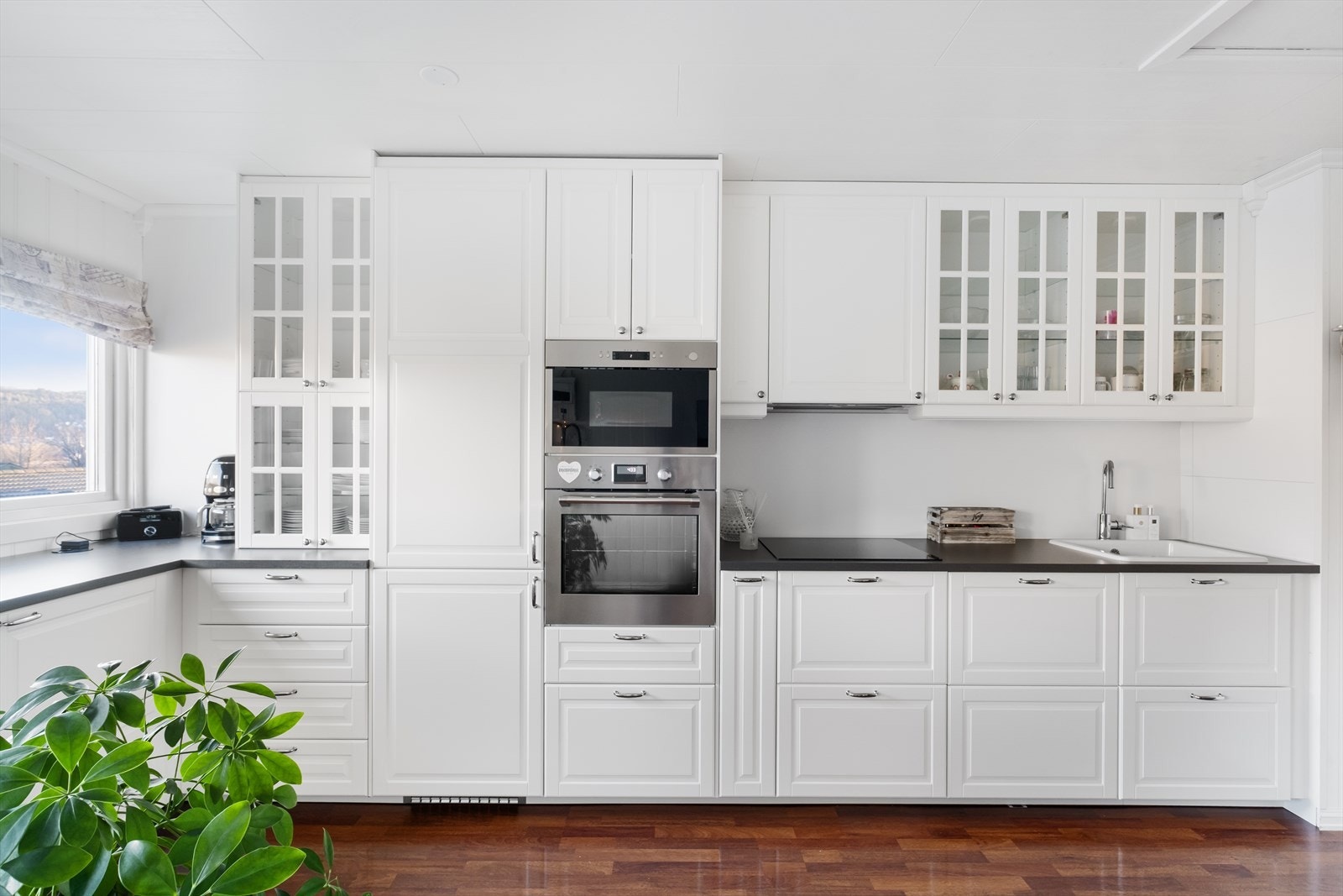 Moderne kjøkken med hvite fronter, innebygd stekeovn og store glassdører som skaper en åpen og elegant atmosfære Galleribilde