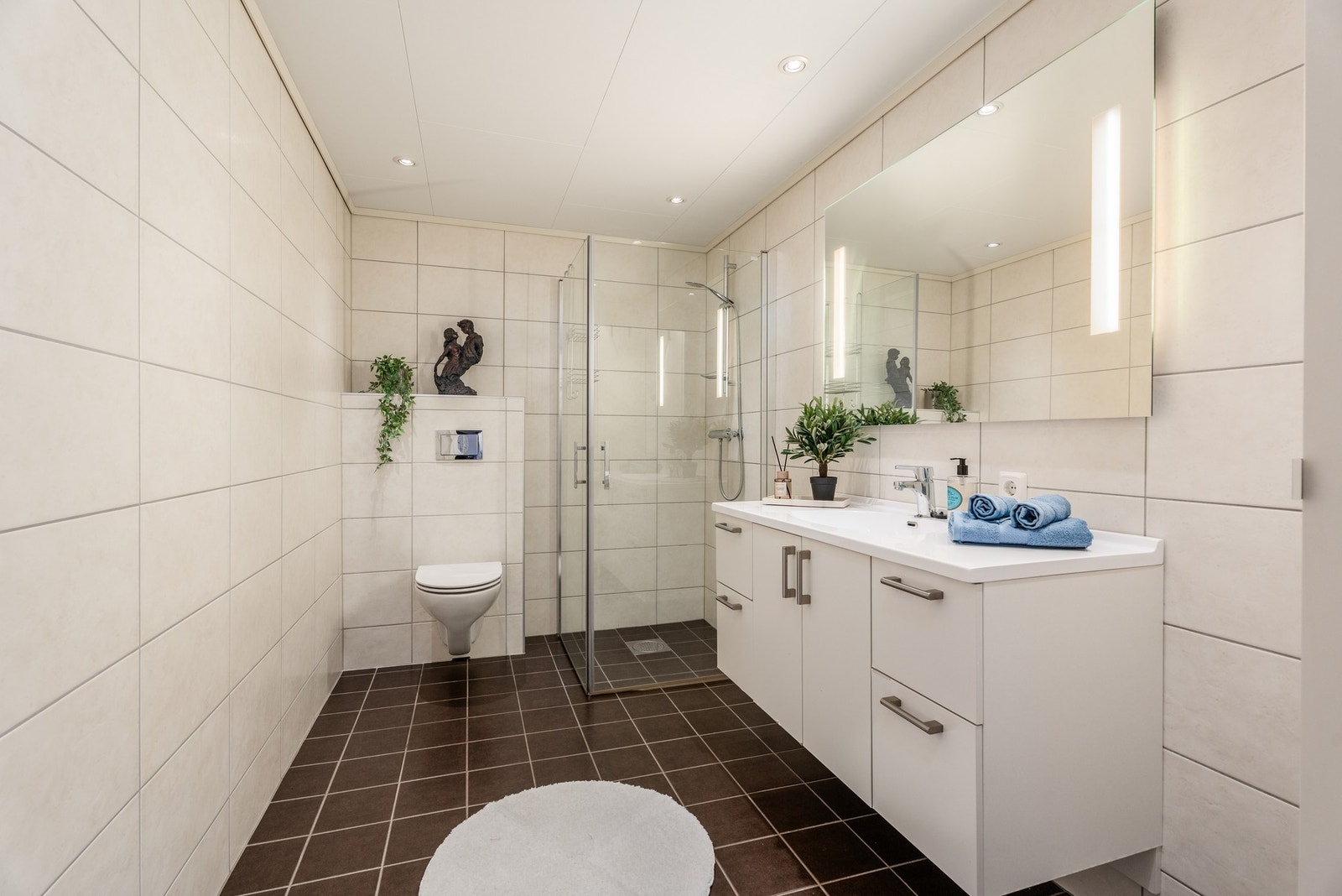 Helfliset og delikat bad med vegghengt toalett og foldedører til dusjnisje. Legg merke til den innholdsrike servantinnredningen og lyssettingen på speilet. Galleribilde