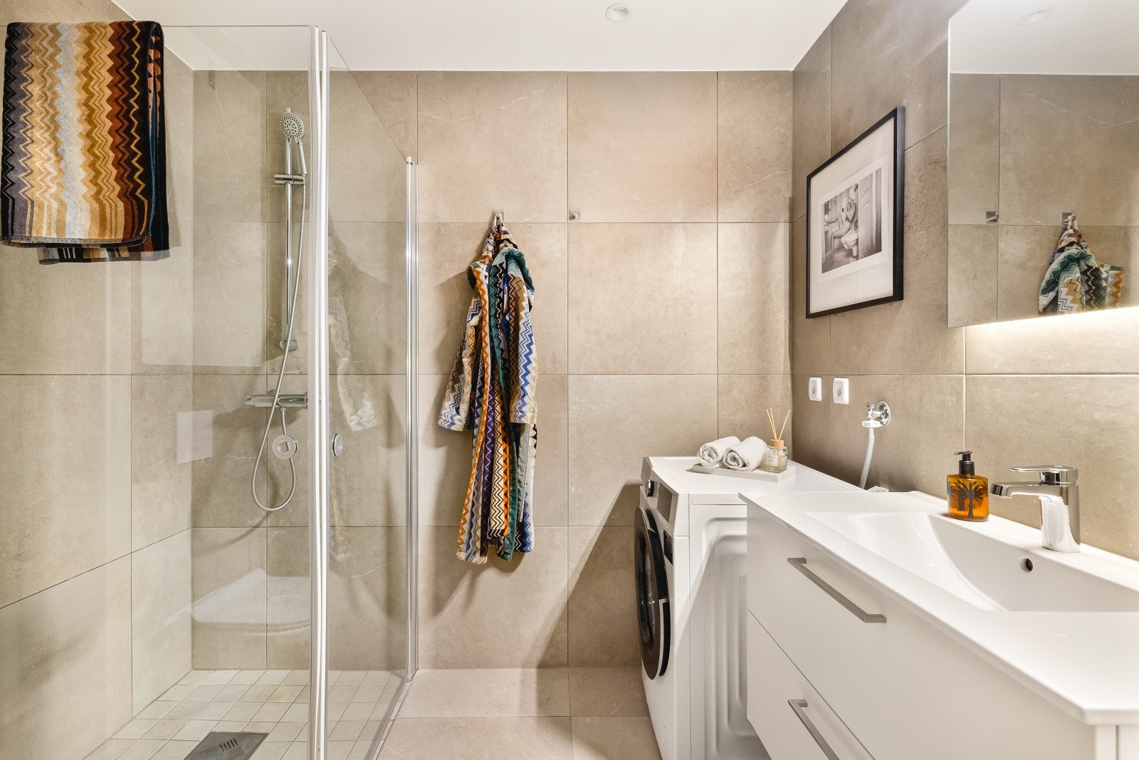 Baderommet måler 4,2 kvm og fremstår moderne og funksjonelt. Rommet er innredet med keramiske fliser på gulv og vegger, kombinert med malt platekledning som gir et rent og tidløst uttrykk. LED-spotlights i himlingen. Galleribilde