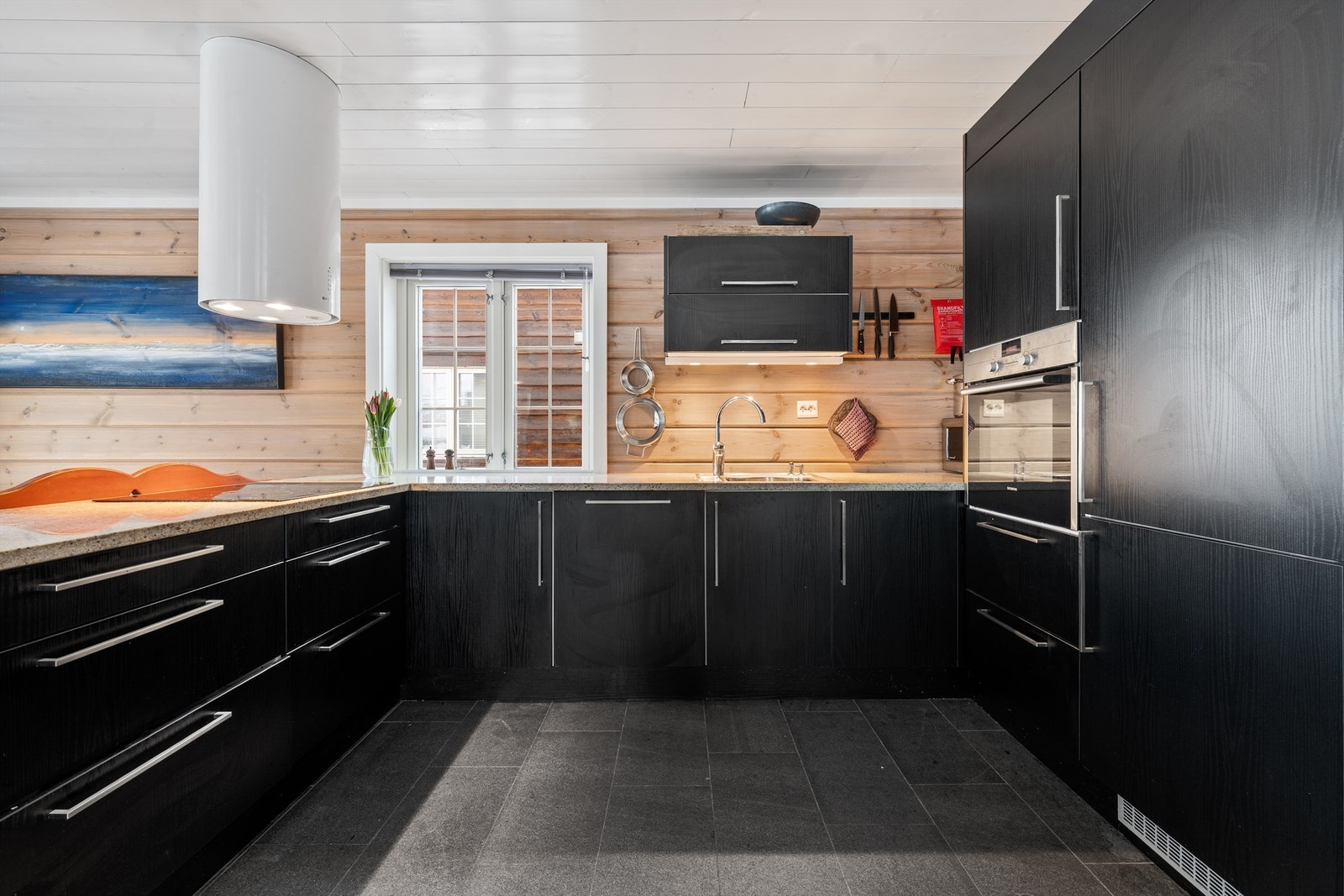 Kjøkkenet er innredet ved byggeår med glatte fronter og benkeplate av stein Galleribilde