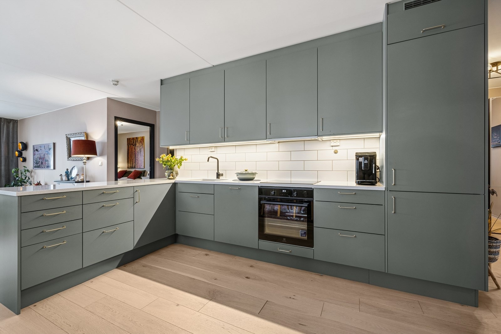 Stilig kjøkkeninnredning med grønne glatte fronter og benkeplate av stein. Hvitevarer er integrerte. Galleribilde