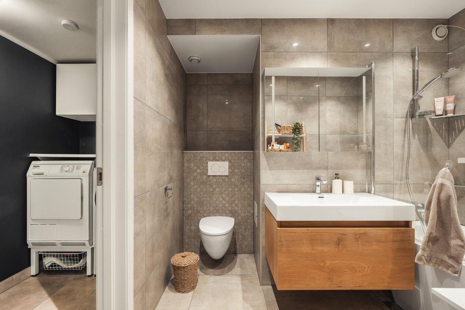 Bad med moderne fliser, vegghengt toalett, dusj og vaskemaskin i tilstøtende rom. Galleribilde